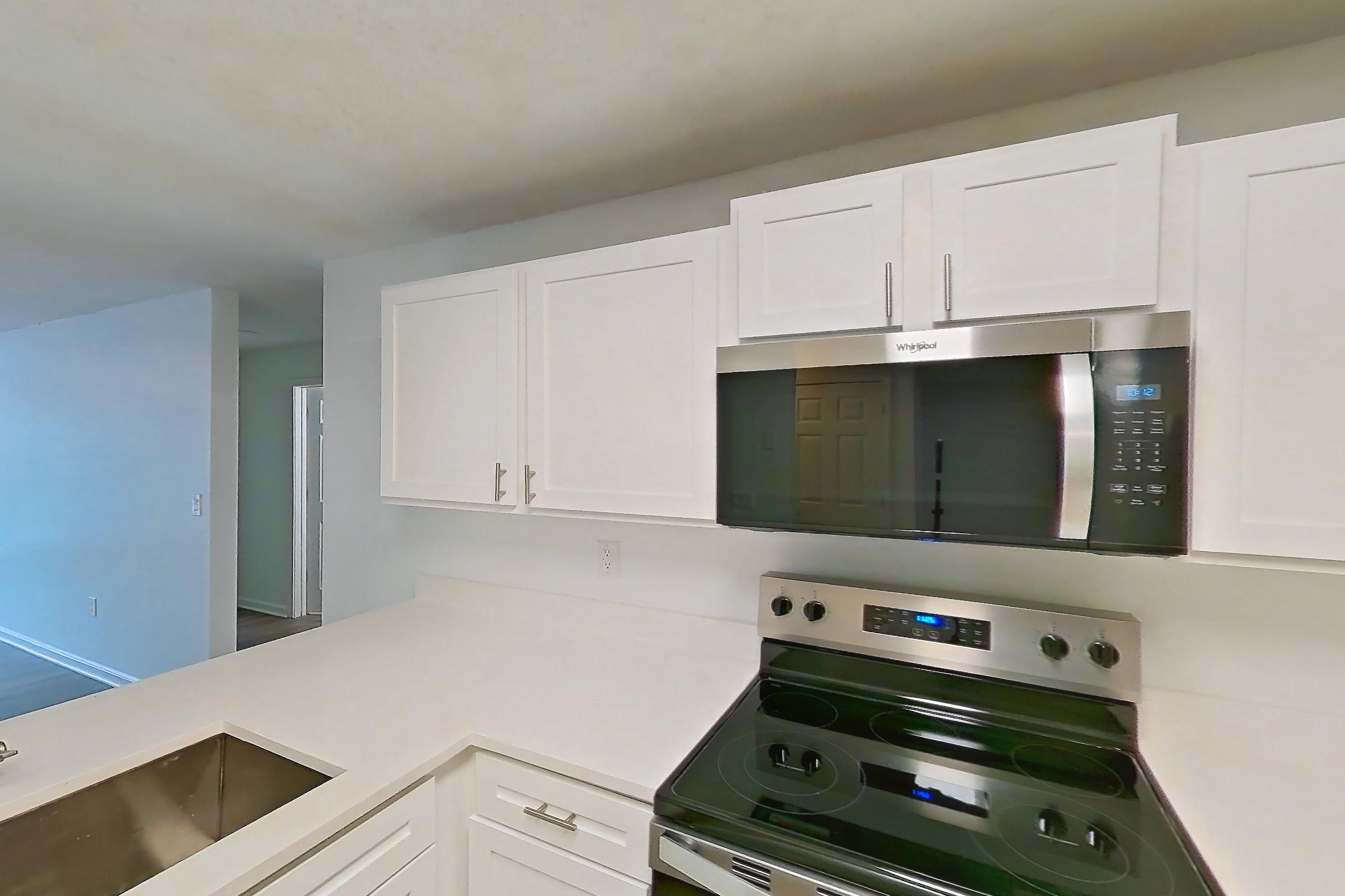 Kitchen with black appliances, dishwasher, electric range, light countertops, light stone countertops, light wood-finish flooring, microwave, oven/range, and stainless steel appliances, Apartment 6415-3H at Ashford Place