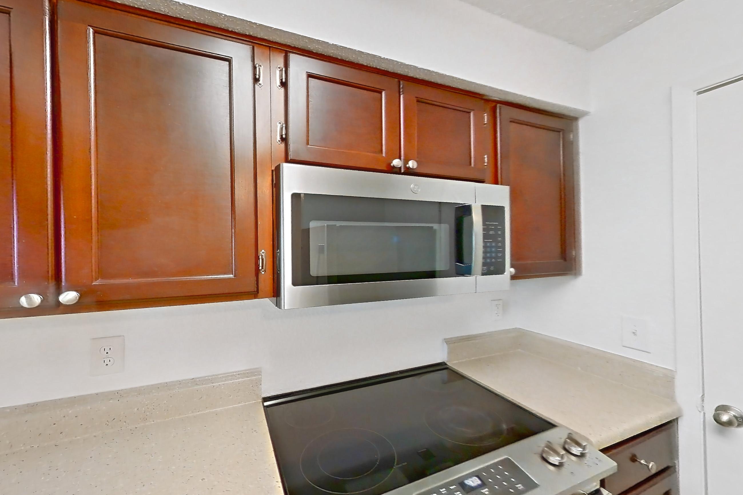 Kitchen with dishwasher, electric range, light countertops, light stone countertops, light wood-finish flooring, microwave, oven/range, refrigerator, and stainless steel appliances, Apartment 10-0109 at Brookwood Club