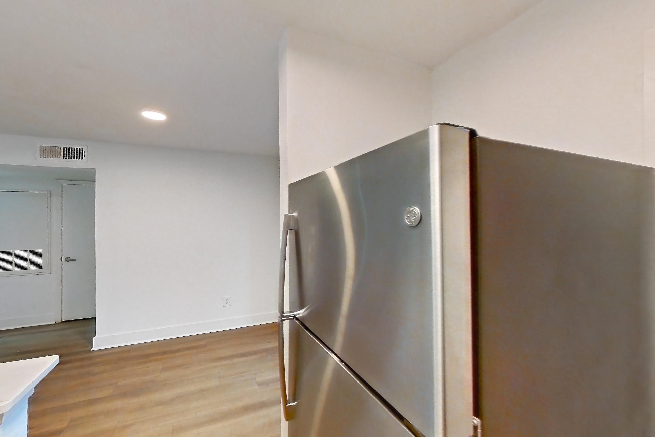 Kitchen with black appliances, electric range, light countertops, light stone countertops, light wood-finish flooring, microwave, oven/range, refrigerator, and stainless steel appliances, Apartment 10-1203 at Brookwood Club