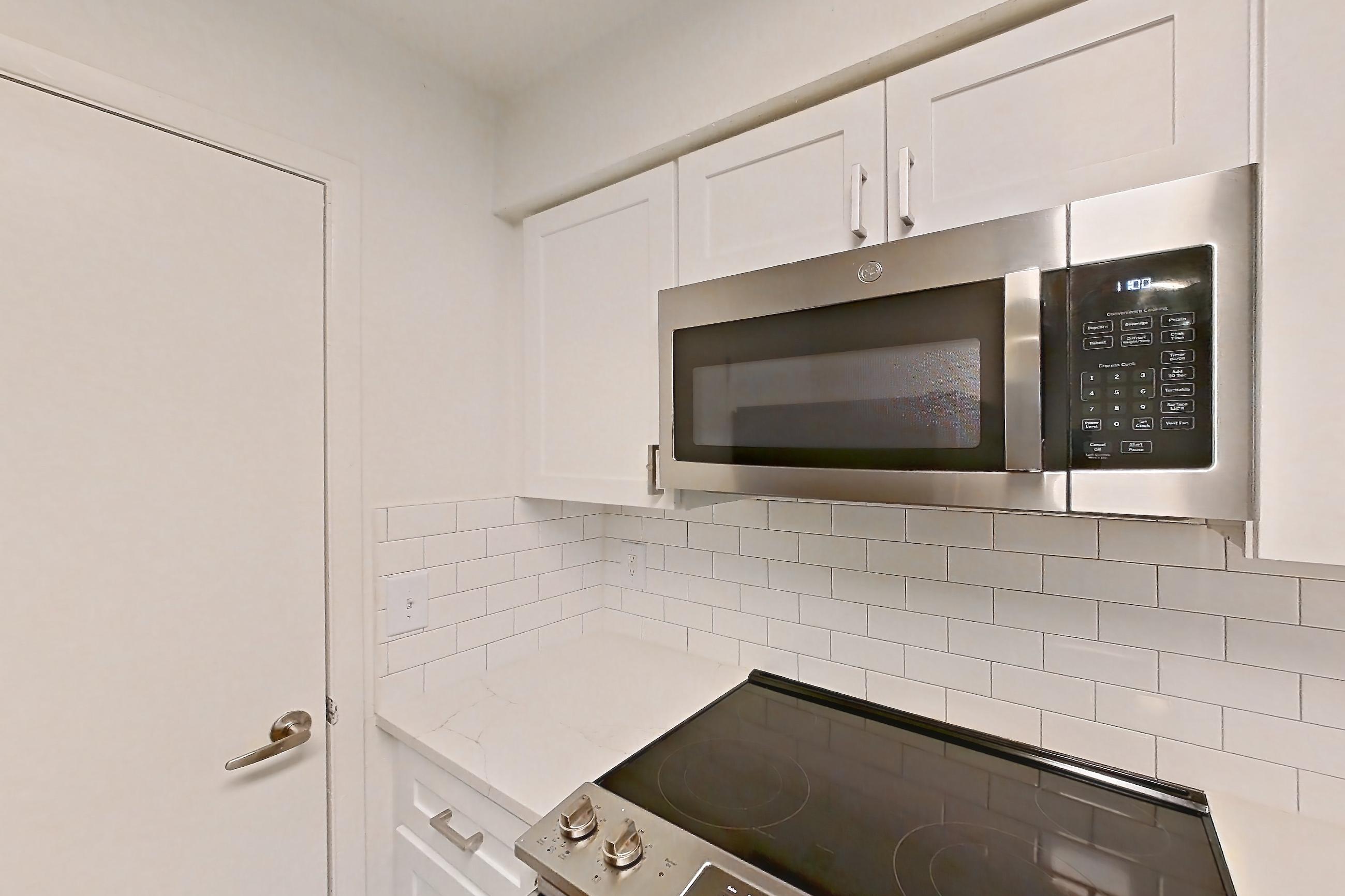 Kitchen with black appliances, electric range, light countertops, light stone countertops, light wood-finish flooring, microwave, oven/range, refrigerator, and stainless steel appliances, Apartment 10-1203 at Brookwood Club