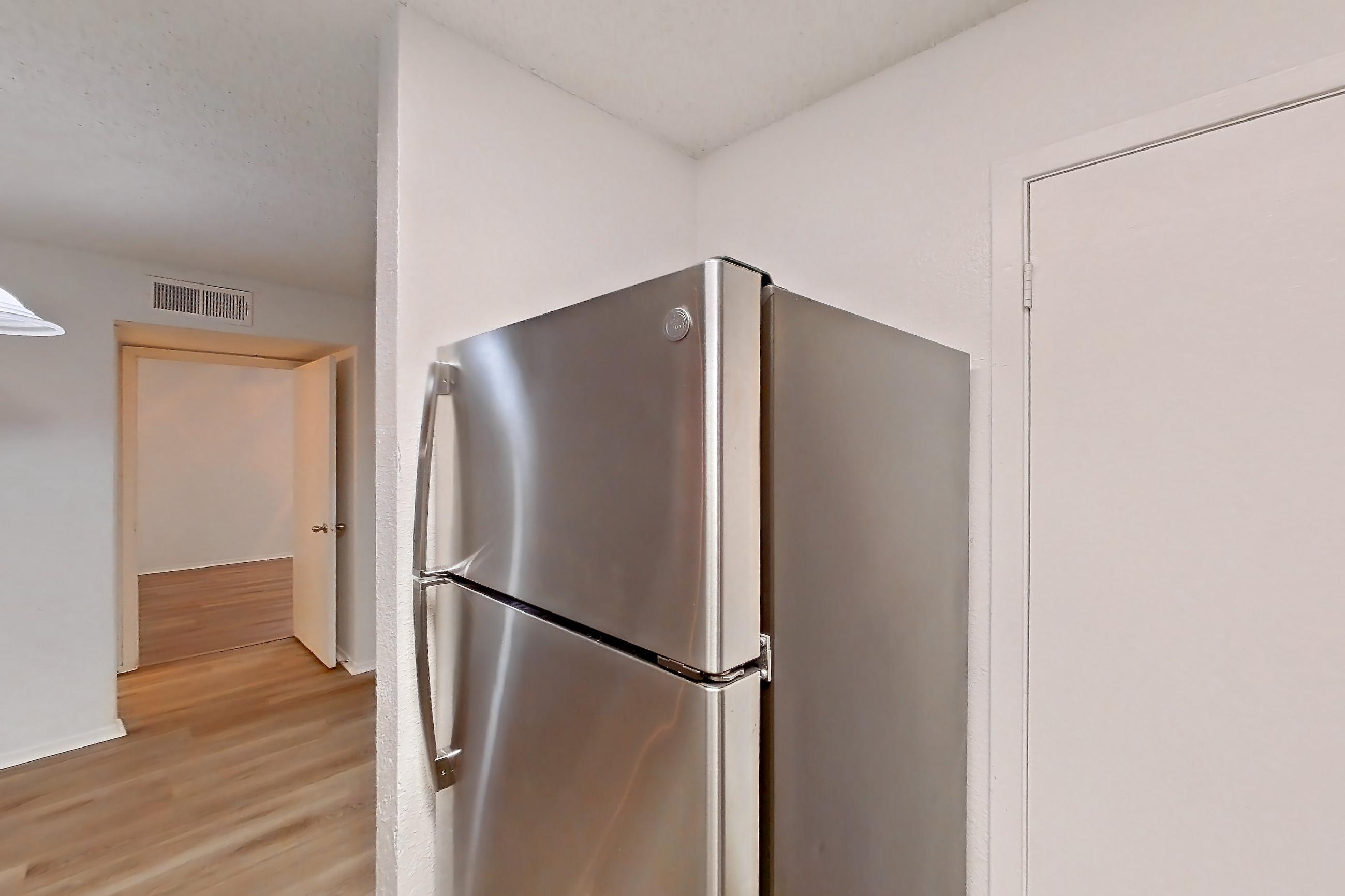 Kitchen with dishwasher, electric range, light countertops, light wood-finish flooring, oven/range, range hood, refrigerator, and stainless steel appliances, Apartment 10-1102 at Brookwood Club