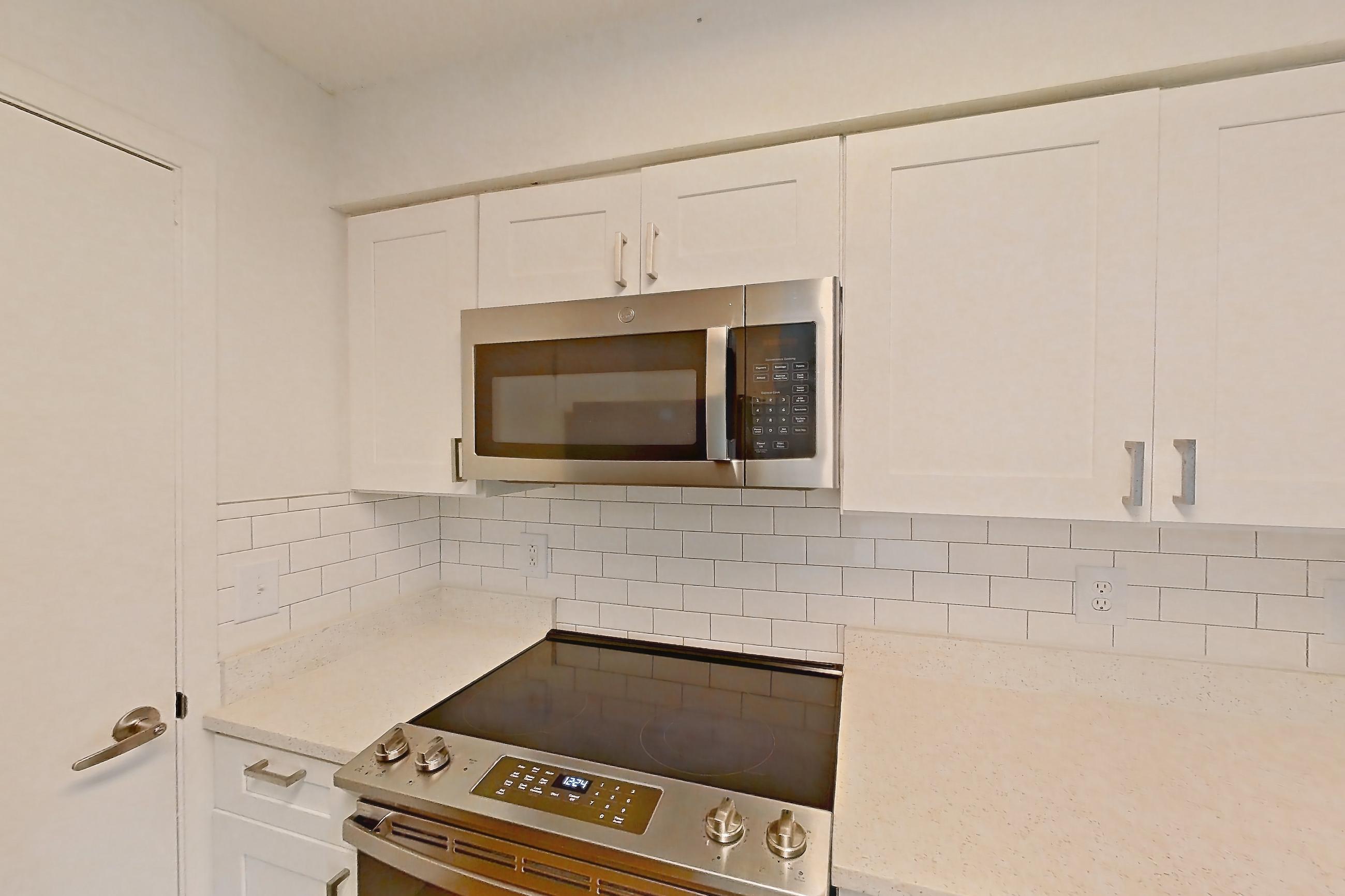Kitchen with dishwasher, electric range, light countertops, light stone countertops, light wood-finish flooring, microwave, oven/range, refrigerator, and stainless steel appliances, Apartment 20-0517 at Brookwood Club