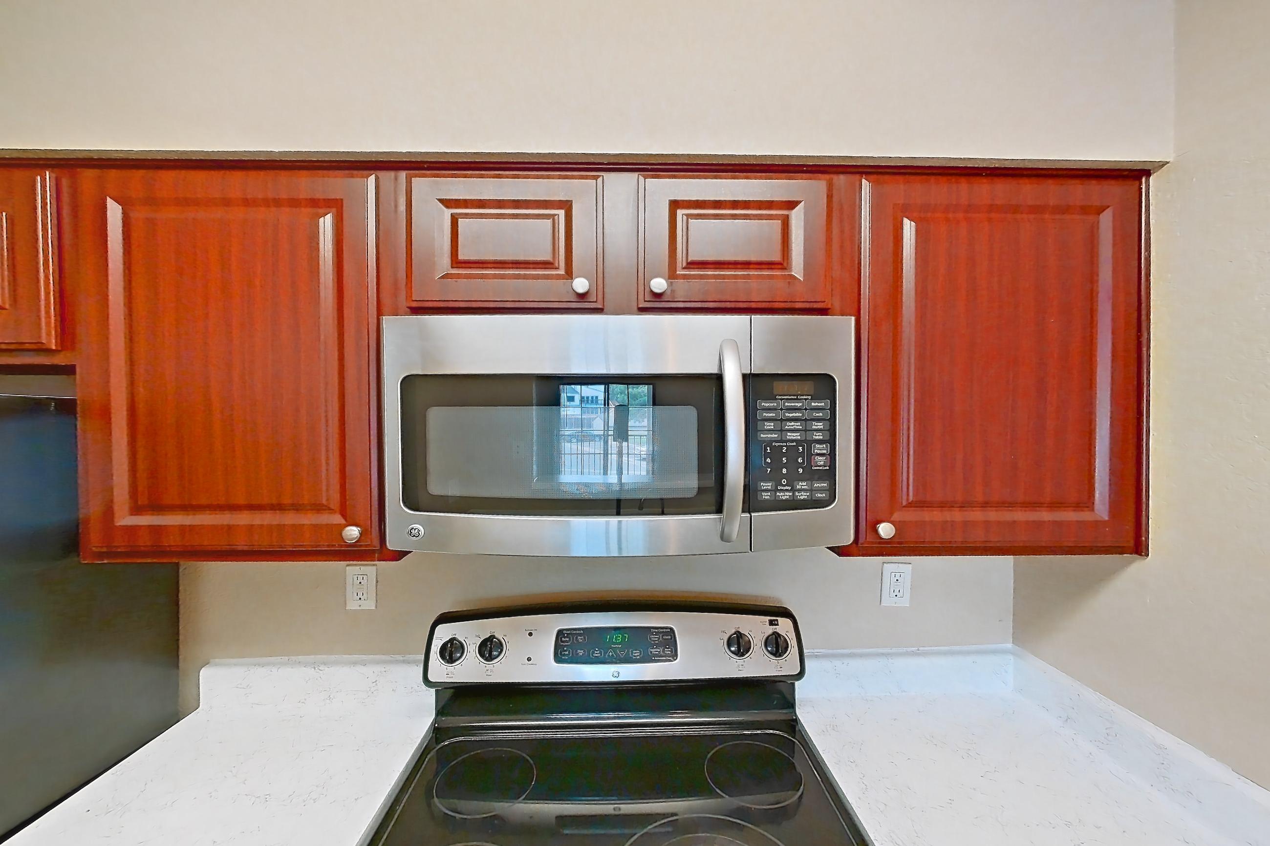 Kitchen with dishwasher, electric range, light countertops, light stone countertops, light wood-finish flooring, microwave, oven/range, refrigerator, and stainless steel appliances, Apartment 3527 at Canyon Chase