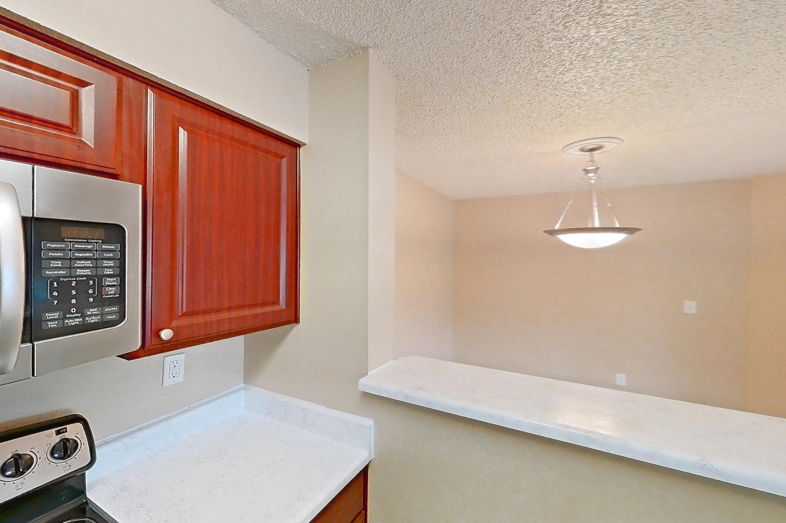 Kitchen with dishwasher, electric range, light countertops, light stone countertops, light wood-finish flooring, microwave, oven/range, refrigerator, and stainless steel appliances, Apartment 3527 at Canyon Chase