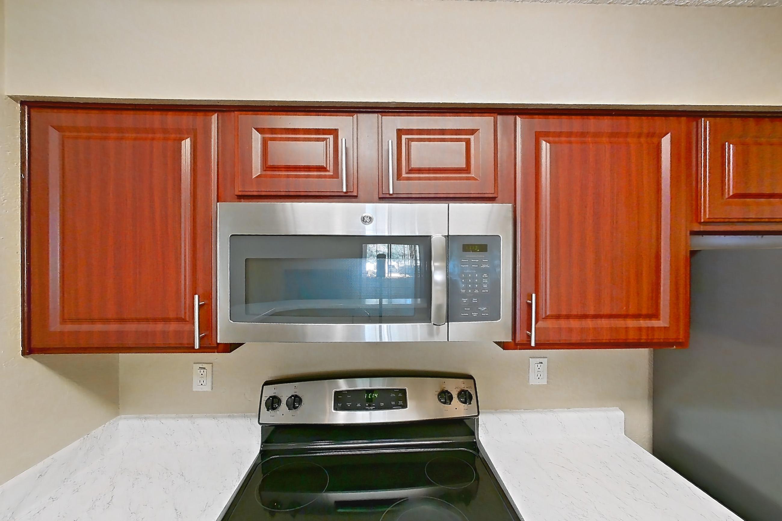 Kitchen with dishwasher, electric range, light countertops, light stone countertops, light wood-finish flooring, microwave, oven/range, refrigerator, and stainless steel appliances, Apartment 3514 at Canyon Chase