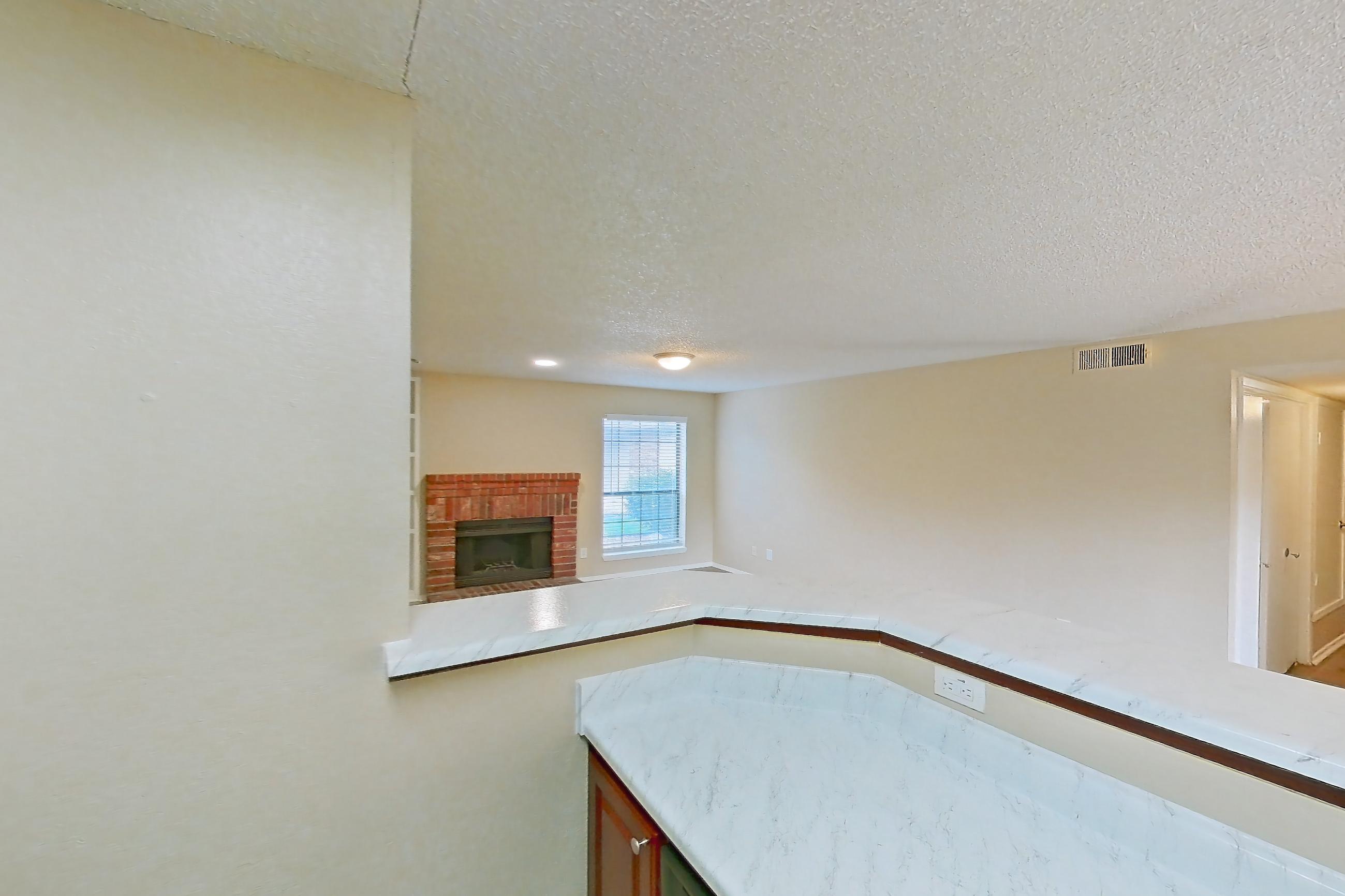 Kitchen with black appliances, brick fireplace, dishwasher, electric range, fireplace, light countertops, light stone countertops, light wood-finish flooring, microwave, oven/range, refrigerator, and stainless steel appliances, Apartment 1812 at Canyon Chase