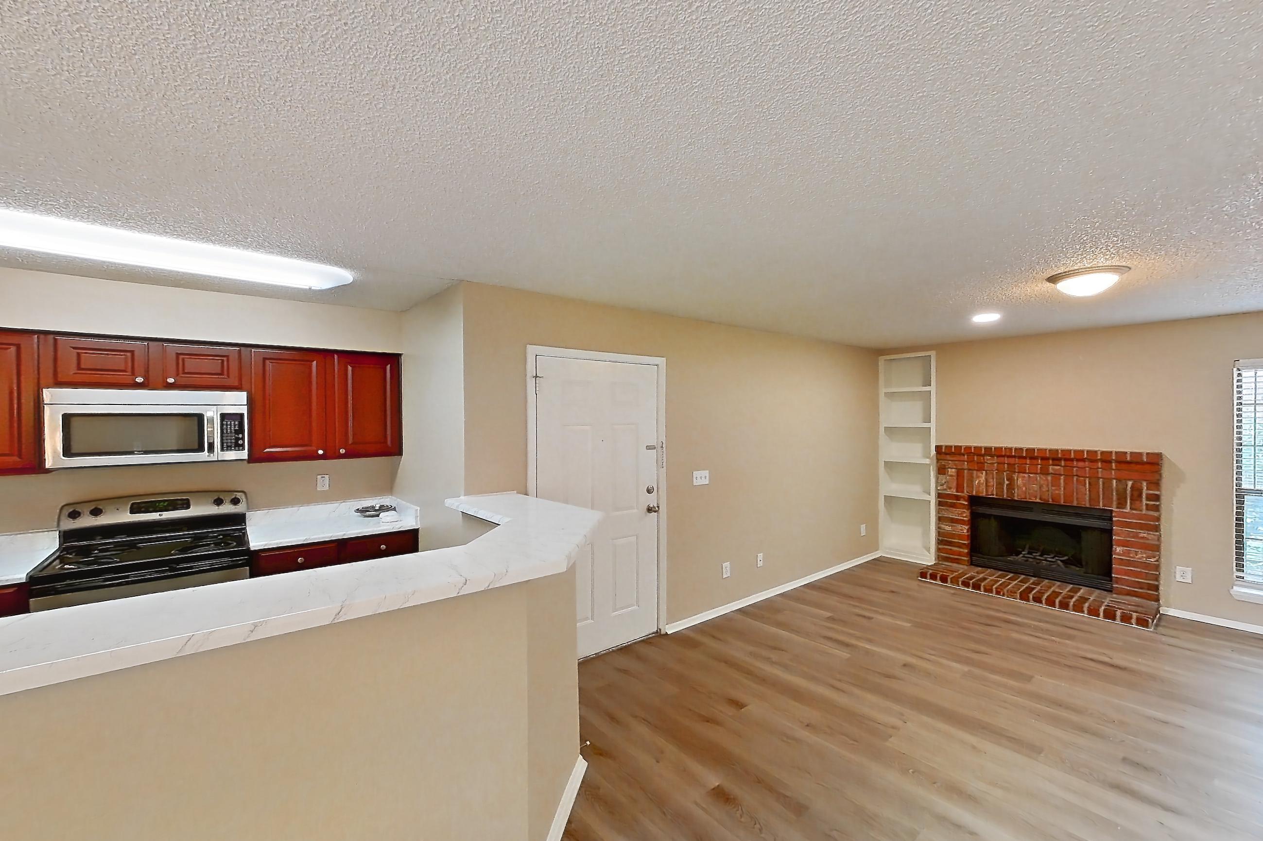 Living space with brick fireplace, fireplace, gas range, light stone countertops, light wood-finish flooring, microwave, oven/range, refrigerator, and stainless steel appliances, Apartment 1812 at Canyon Chase