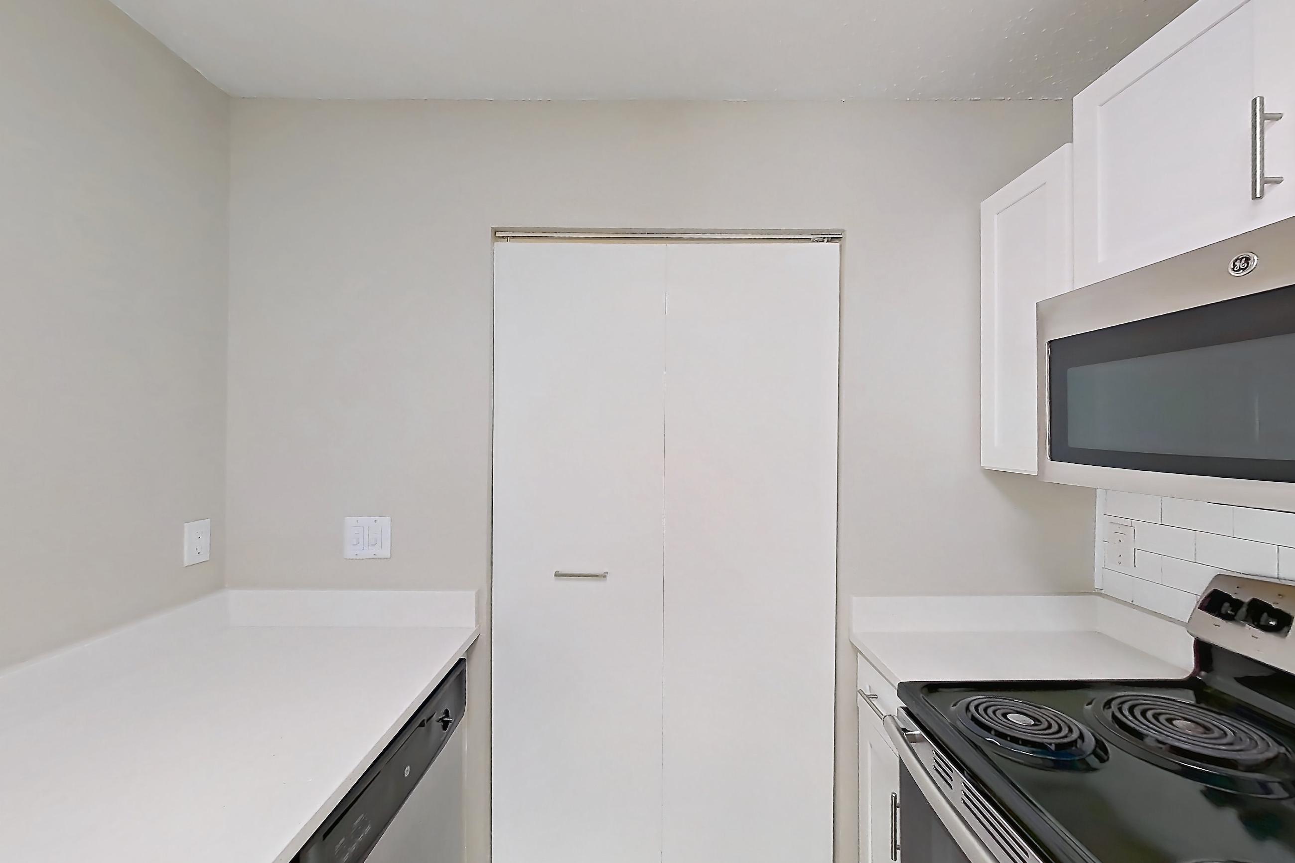 Kitchen with dishwasher, electric range, light countertops, light stone countertops, light wood-finish flooring, microwave, oven/range, and stainless steel appliances, Apartment 61-I08 at Crosstown at Chapel Hill
