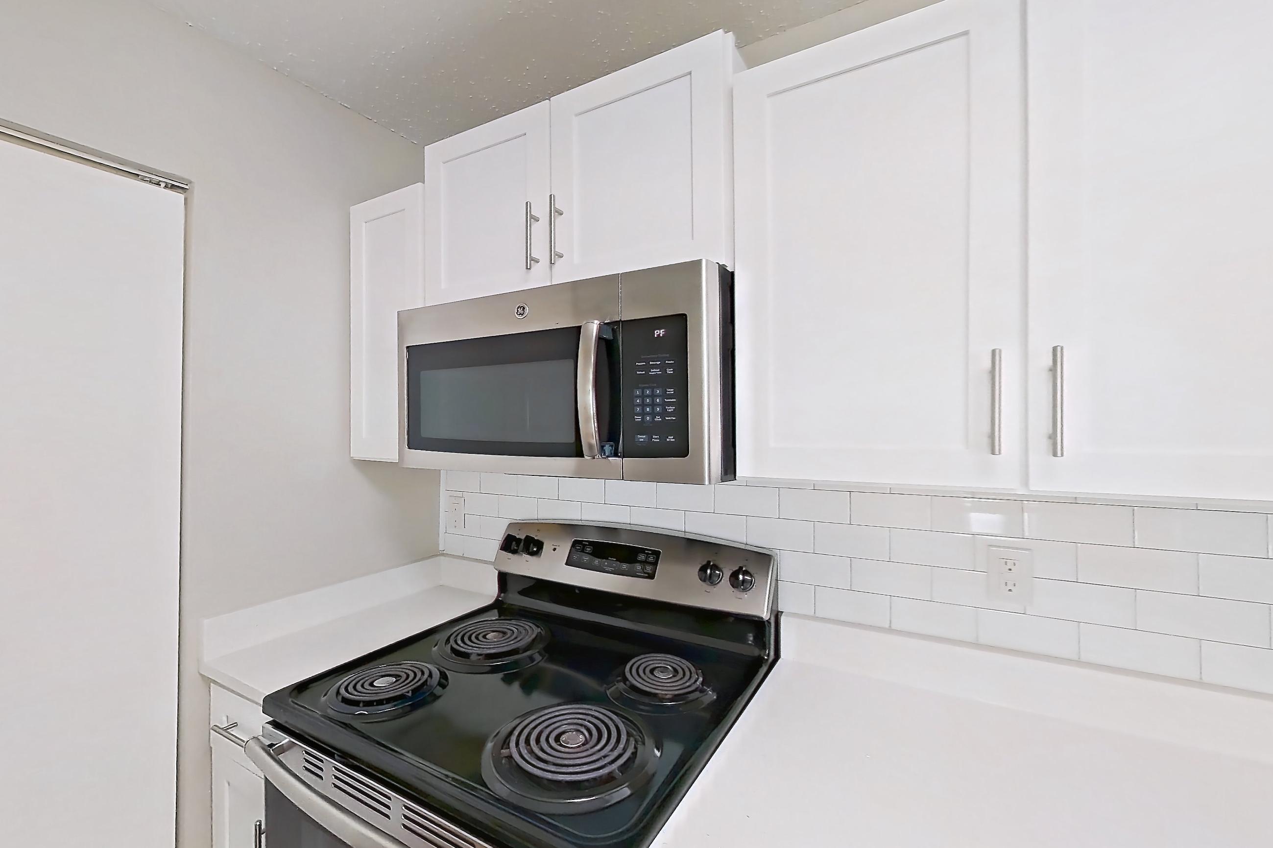 Kitchen with dishwasher, electric range, light countertops, light stone countertops, light wood-finish flooring, microwave, oven/range, and stainless steel appliances, Apartment 61-I08 at Crosstown at Chapel Hill