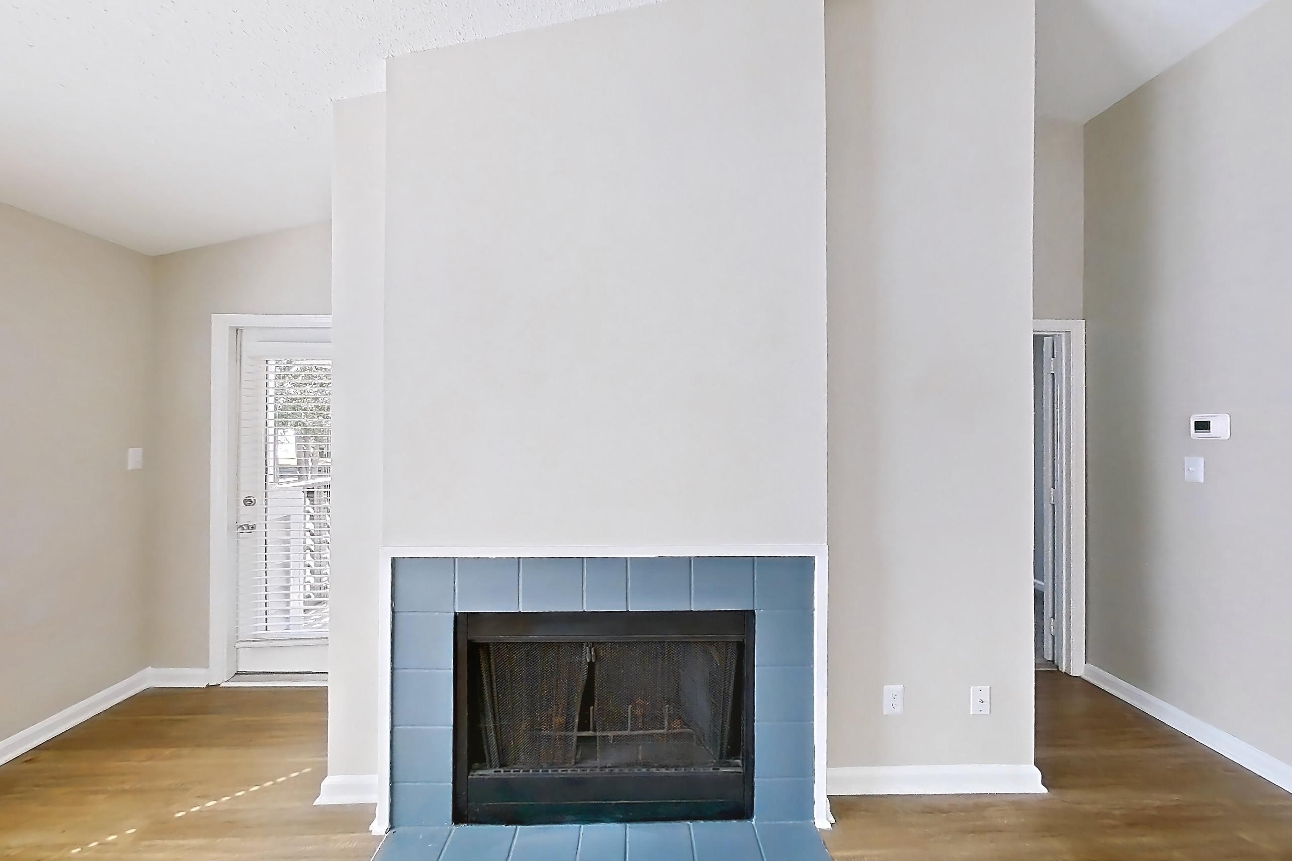 Living room with fireplace, light wood-finish flooring, refrigerator, stainless steel appliances, and tile fireplace, Apartment 61-I08 at Crosstown at Chapel Hill
