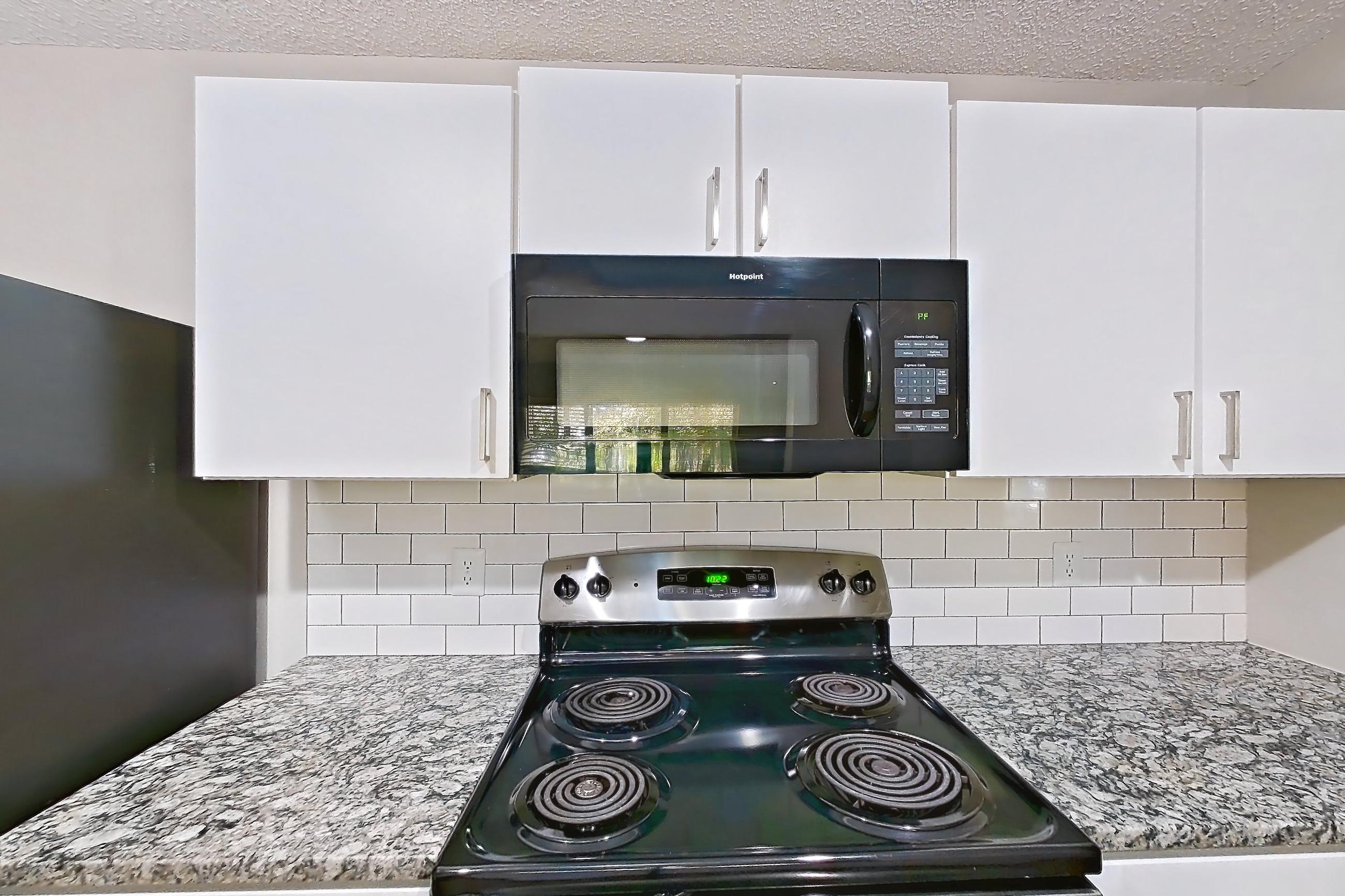 Kitchen with black appliances, dishwasher, electric range, light countertops, light stone countertops, light wood-finish flooring, microwave, oven/range, refrigerator, and stainless steel appliances, Apartment 62-D08 at Crosstown at Chapel Hill