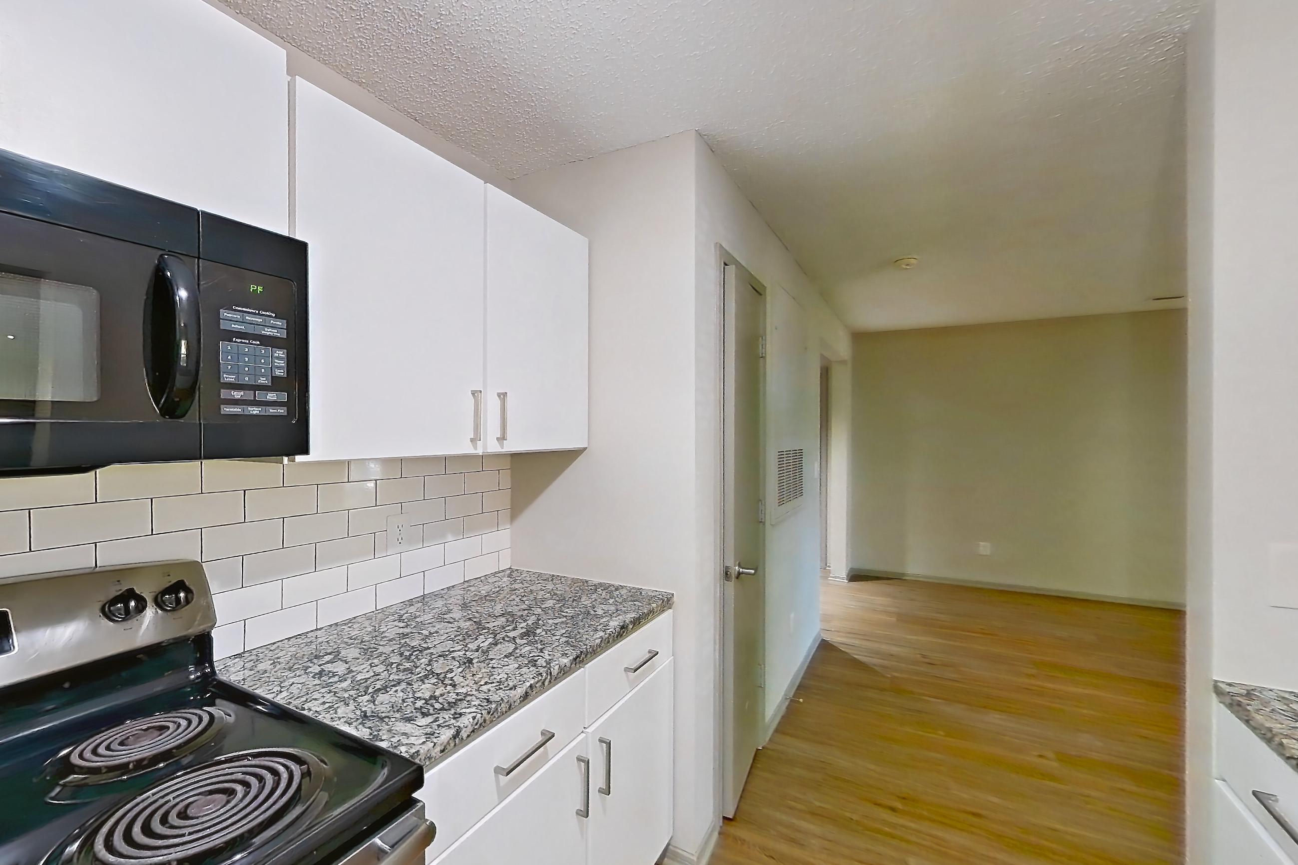Kitchen with black appliances, dishwasher, electric range, light countertops, light stone countertops, light wood-finish flooring, microwave, oven/range, refrigerator, and stainless steel appliances, Apartment 62-D08 at Crosstown at Chapel Hill