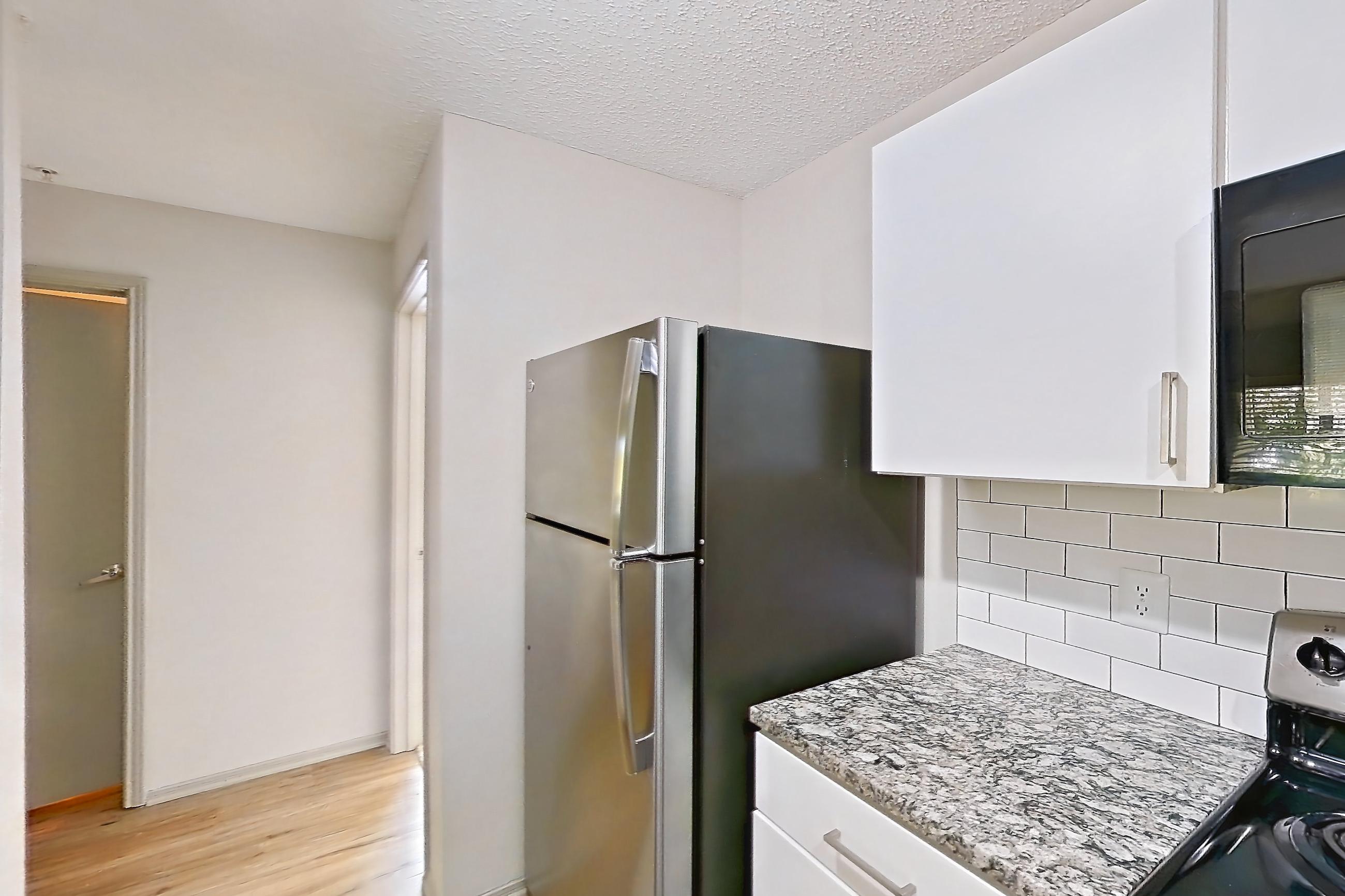 Kitchen with black appliances, dishwasher, electric range, light countertops, light stone countertops, light wood-finish flooring, microwave, oven/range, refrigerator, and stainless steel appliances, Apartment 62-D08 at Crosstown at Chapel Hill