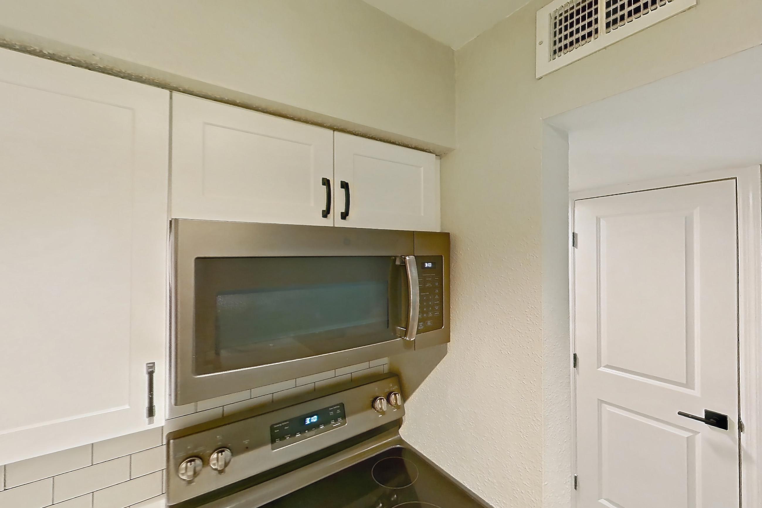 Kitchen with dishwasher, electric range, light countertops, light stone countertops, light wood-finish flooring, microwave, oven/range, refrigerator, and stainless steel appliances, Apartment 04-204 at St. James Crossing