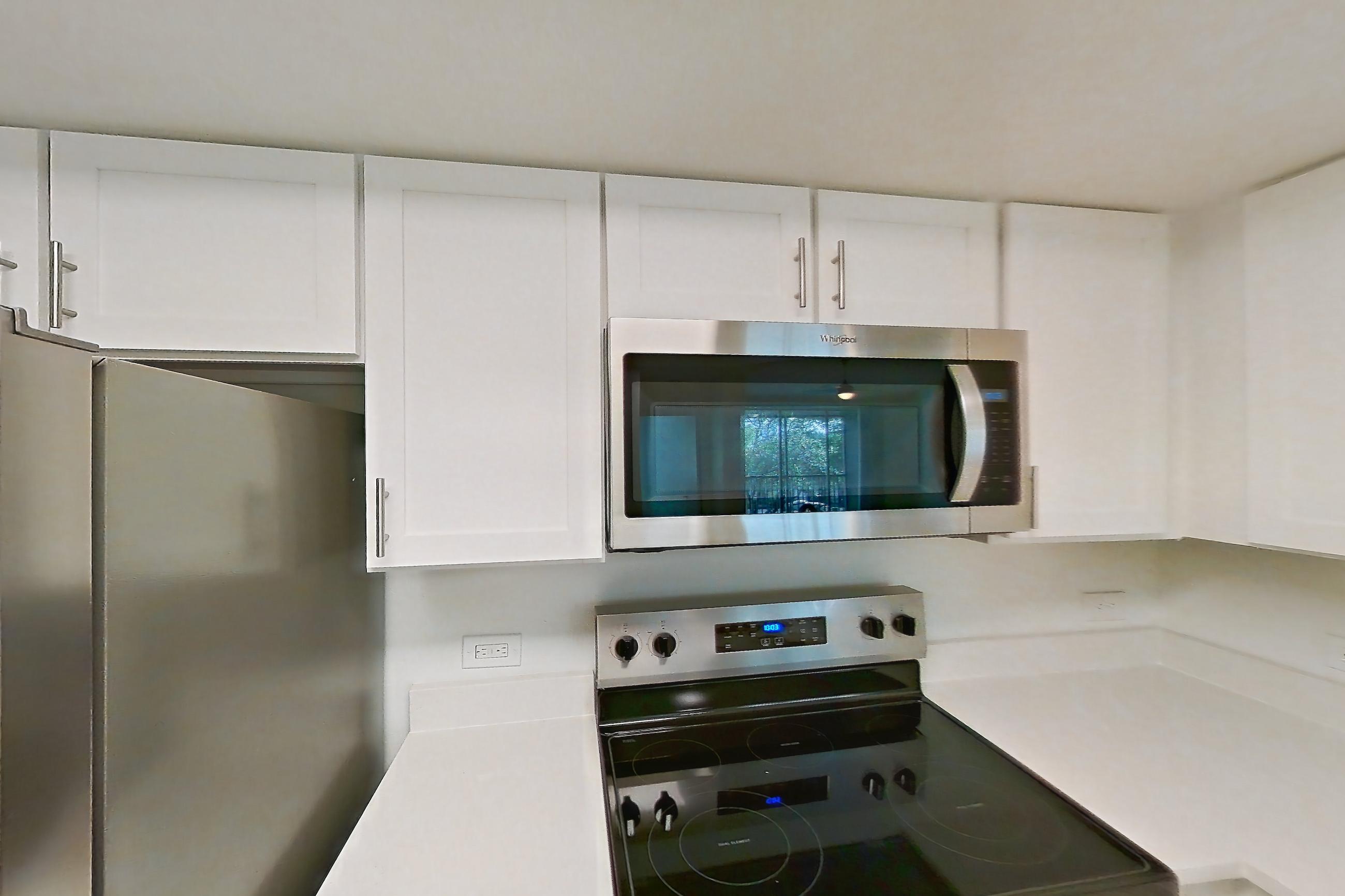 Kitchen with dishwasher, electric range, light countertops, light stone countertops, light tile flooring, microwave, oven/range, and stainless steel appliances, Apartment 09-12234 at Sabal Pointe