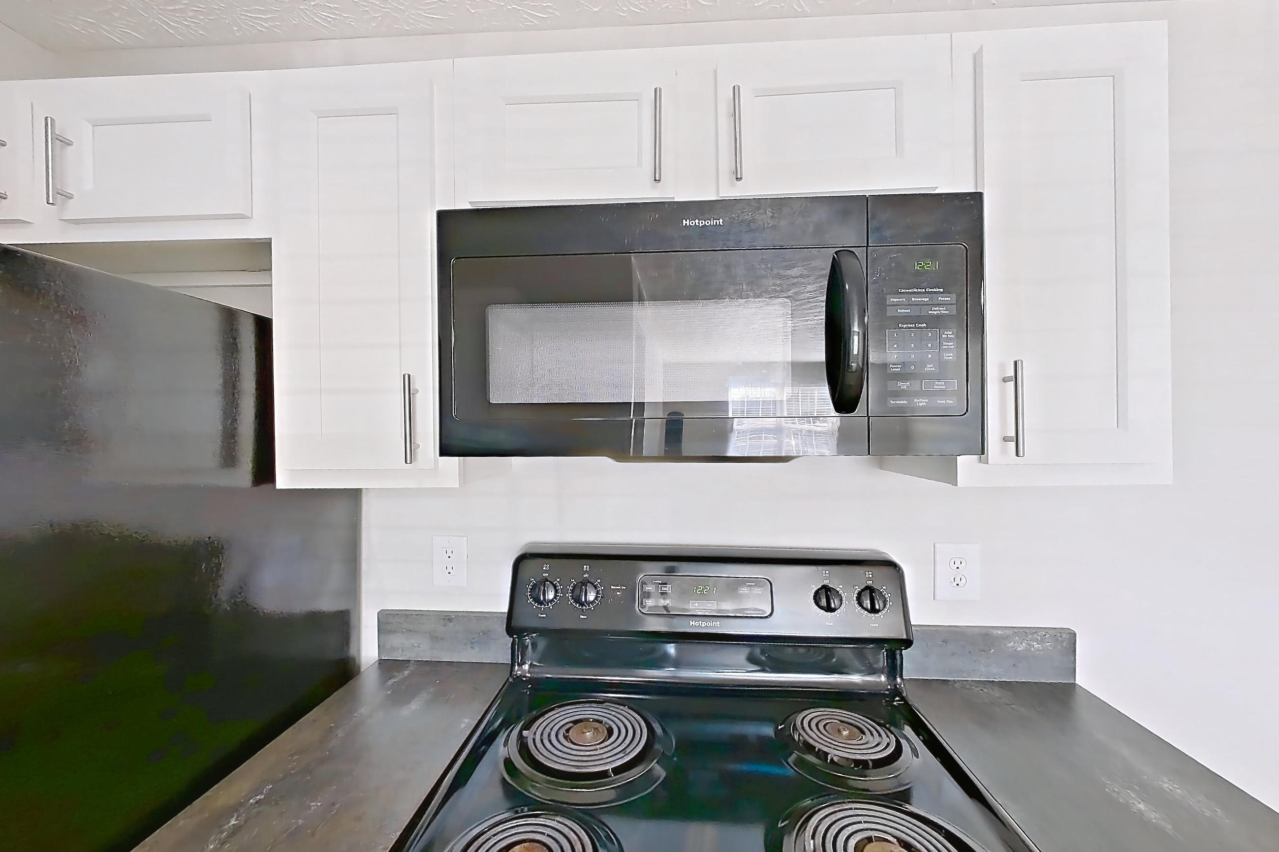 Kitchen with black appliances, dark countertops, dishwasher, electric range, in-unit laundry, light countertops, light wood-finish flooring, microwave, oven/range, refrigerator, and stainless steel appliances, Apartment 2728CLD at The Gardens Columbus