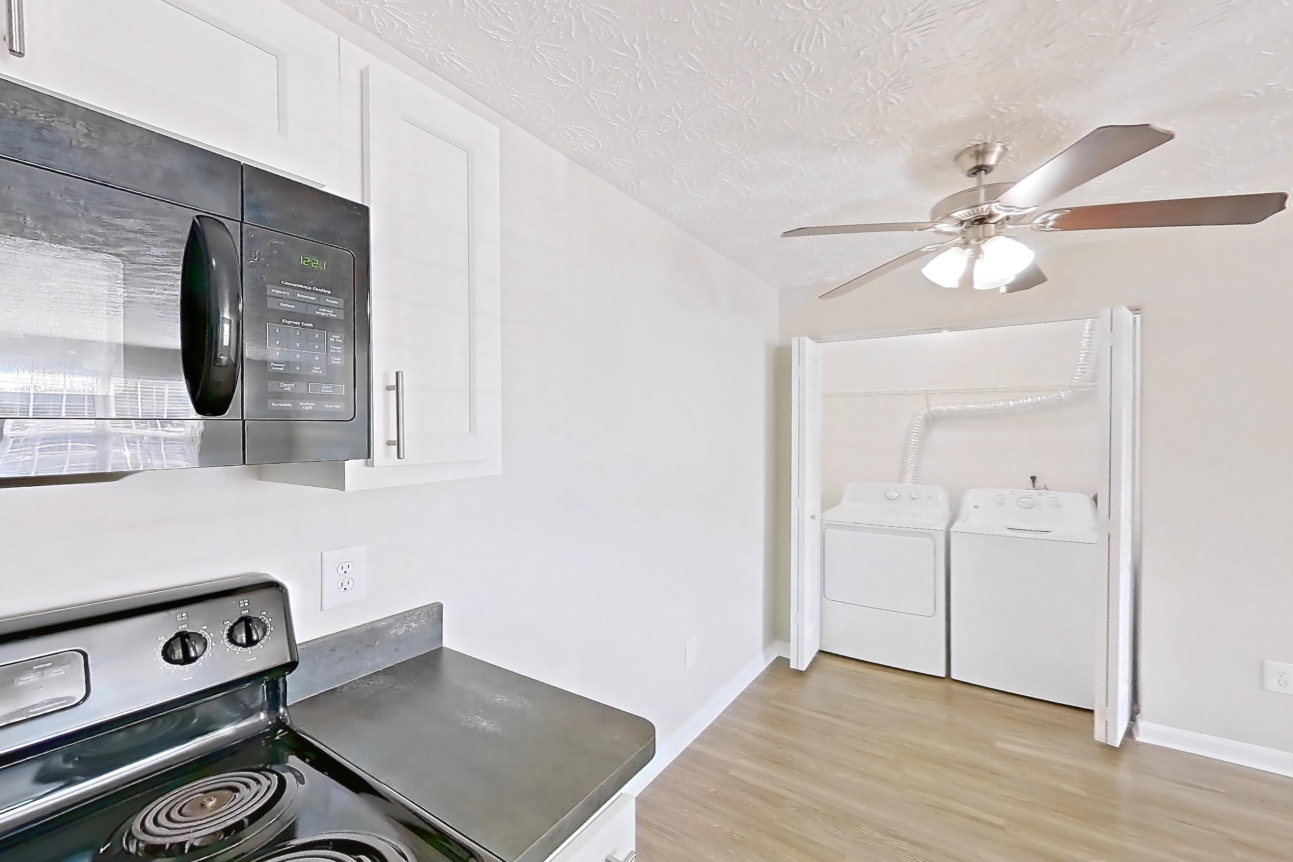 Kitchen with black appliances, dark countertops, dishwasher, electric range, in-unit laundry, light countertops, light wood-finish flooring, microwave, oven/range, refrigerator, and stainless steel appliances, Apartment 2728CLD at The Gardens Columbus