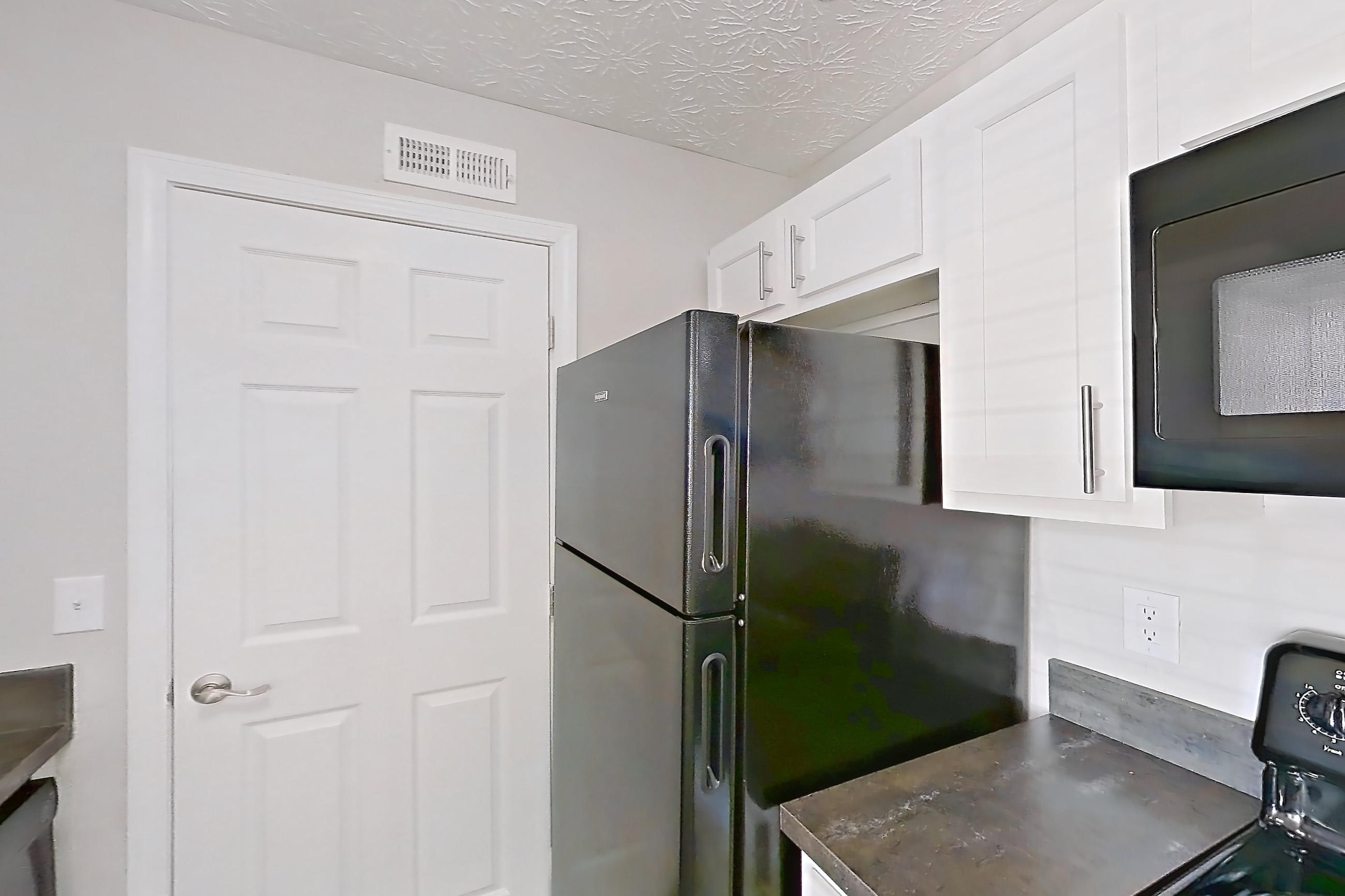 Kitchen with black appliances, dark countertops, dishwasher, electric range, in-unit laundry, light countertops, light wood-finish flooring, microwave, oven/range, refrigerator, and stainless steel appliances, Apartment 2728CLD at The Gardens Columbus