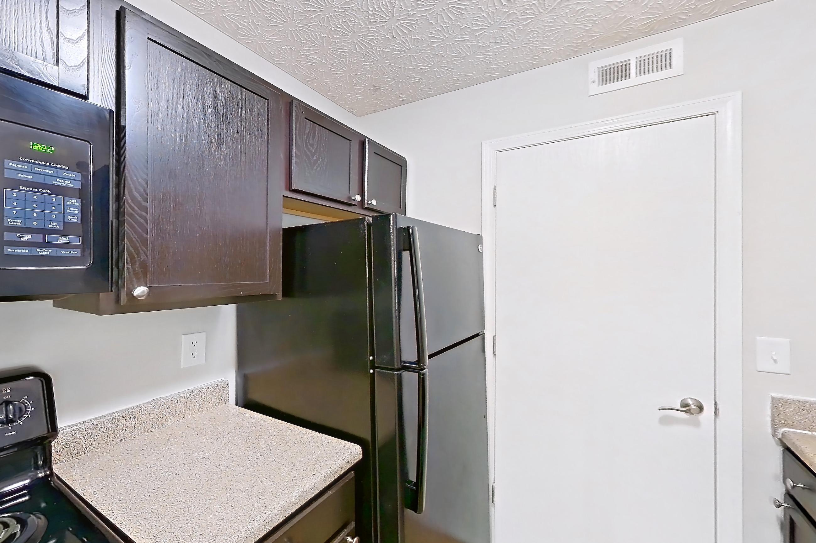 Kitchen with black appliances, dishwasher, electric range, in-unit laundry, light countertops, light wood-finish flooring, microwave, oven/range, and refrigerator, Apartment 3757SLC at The Gardens Columbus