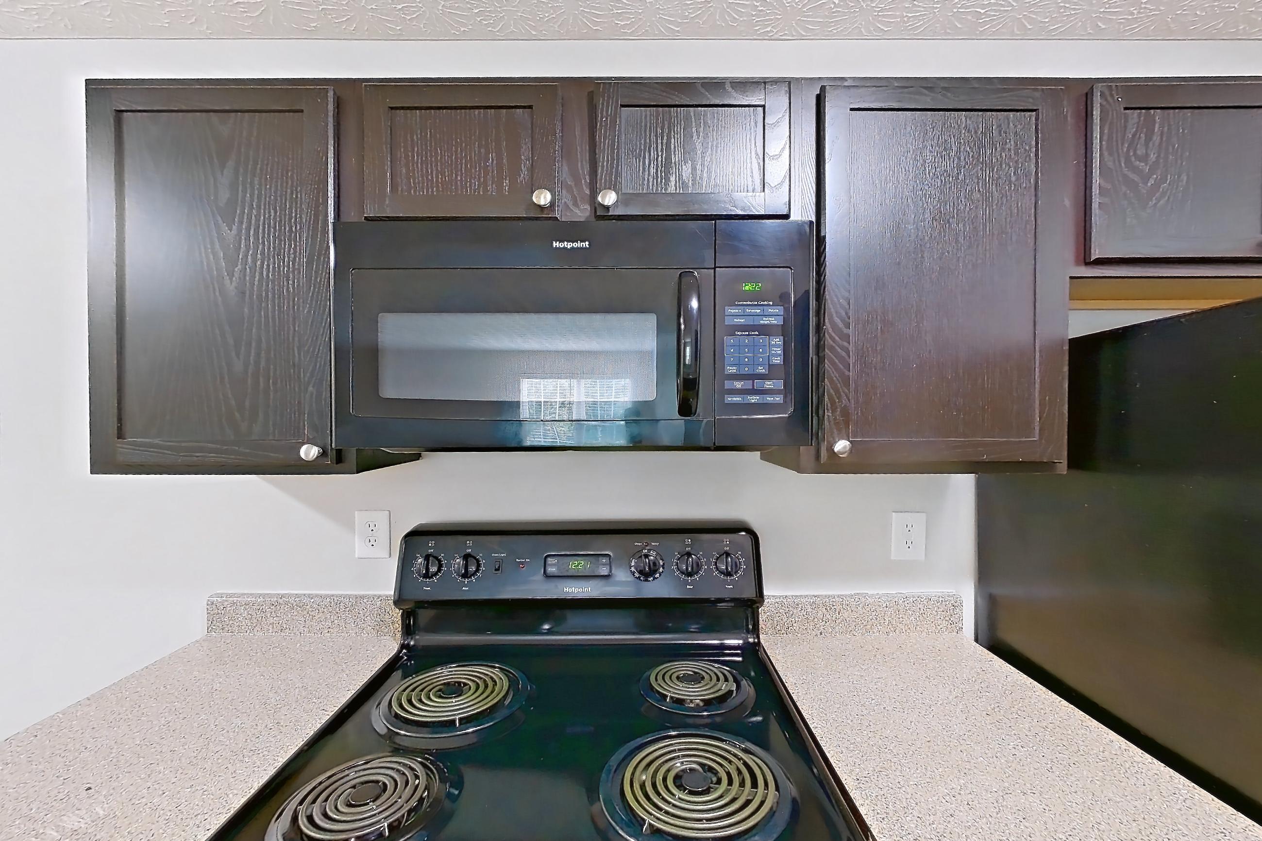Kitchen with black appliances, dishwasher, electric range, in-unit laundry, light countertops, light wood-finish flooring, microwave, oven/range, and refrigerator, Apartment 3757SLC at The Gardens Columbus