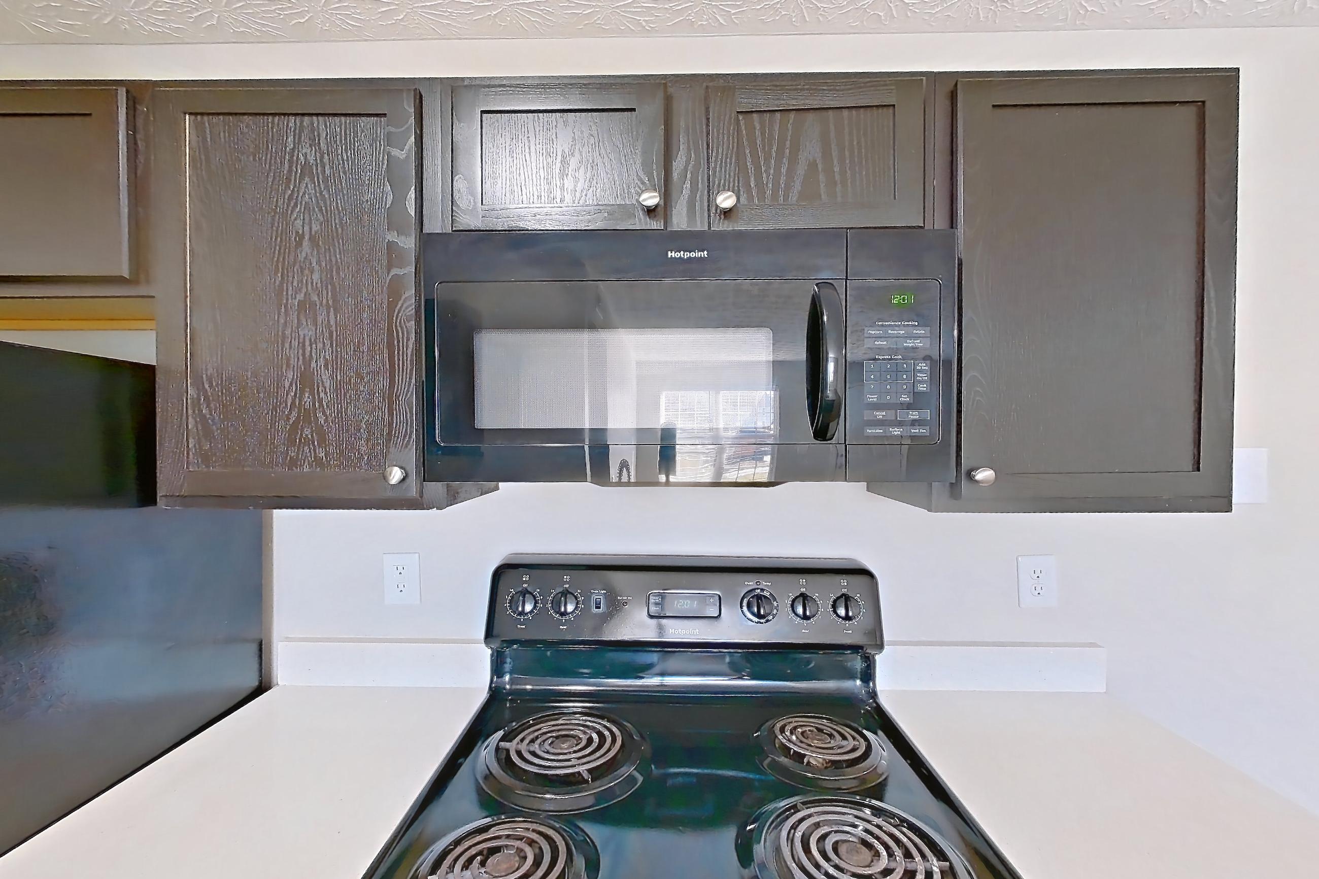 Kitchen with black appliances, dishwasher, electric range, light countertops, light stone countertops, light wood-finish flooring, microwave, oven/range, and refrigerator, Apartment 3152BLD at The Gardens Columbus
