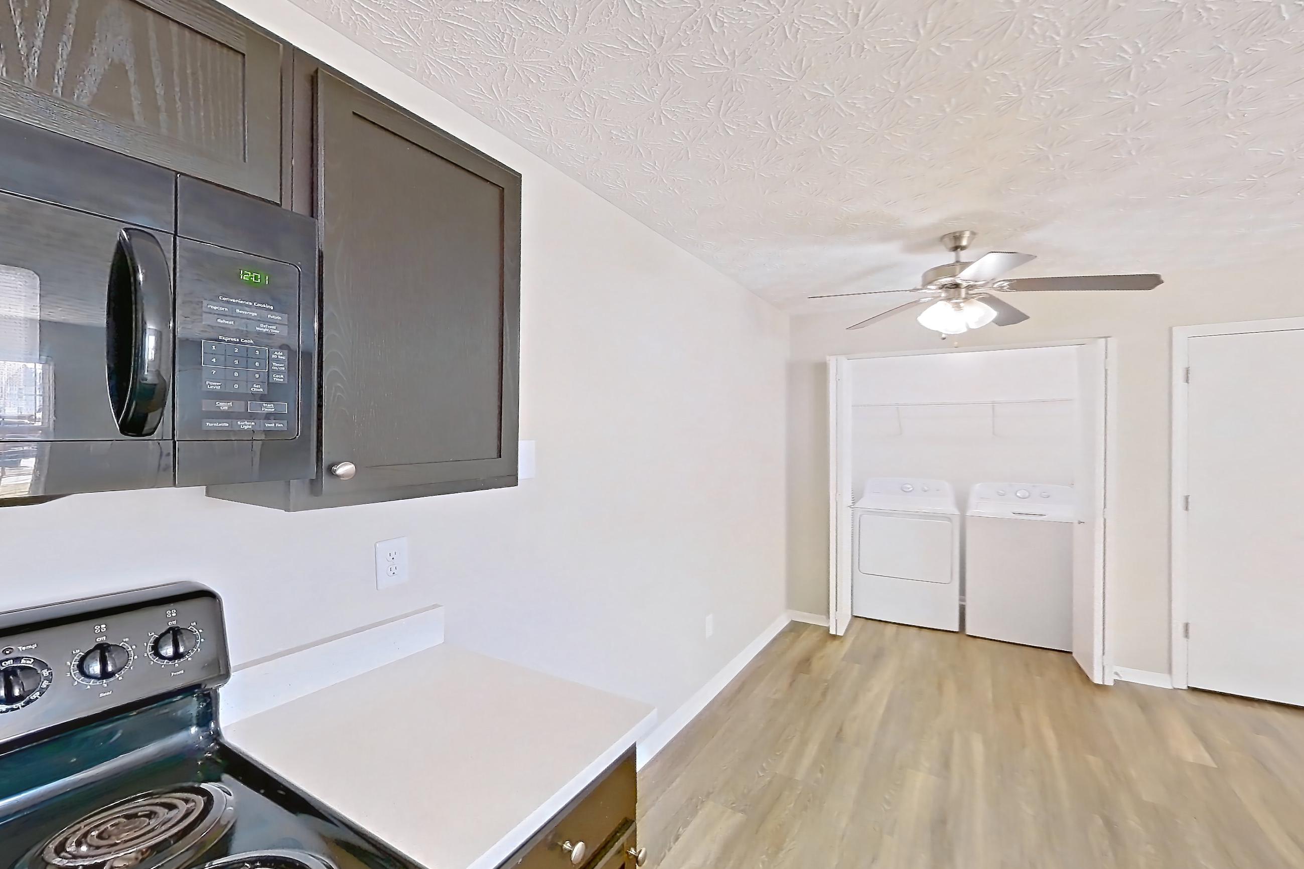 Kitchen with black appliances, dishwasher, electric range, light countertops, light stone countertops, light wood-finish flooring, microwave, oven/range, and refrigerator, Apartment 3152BLD at The Gardens Columbus