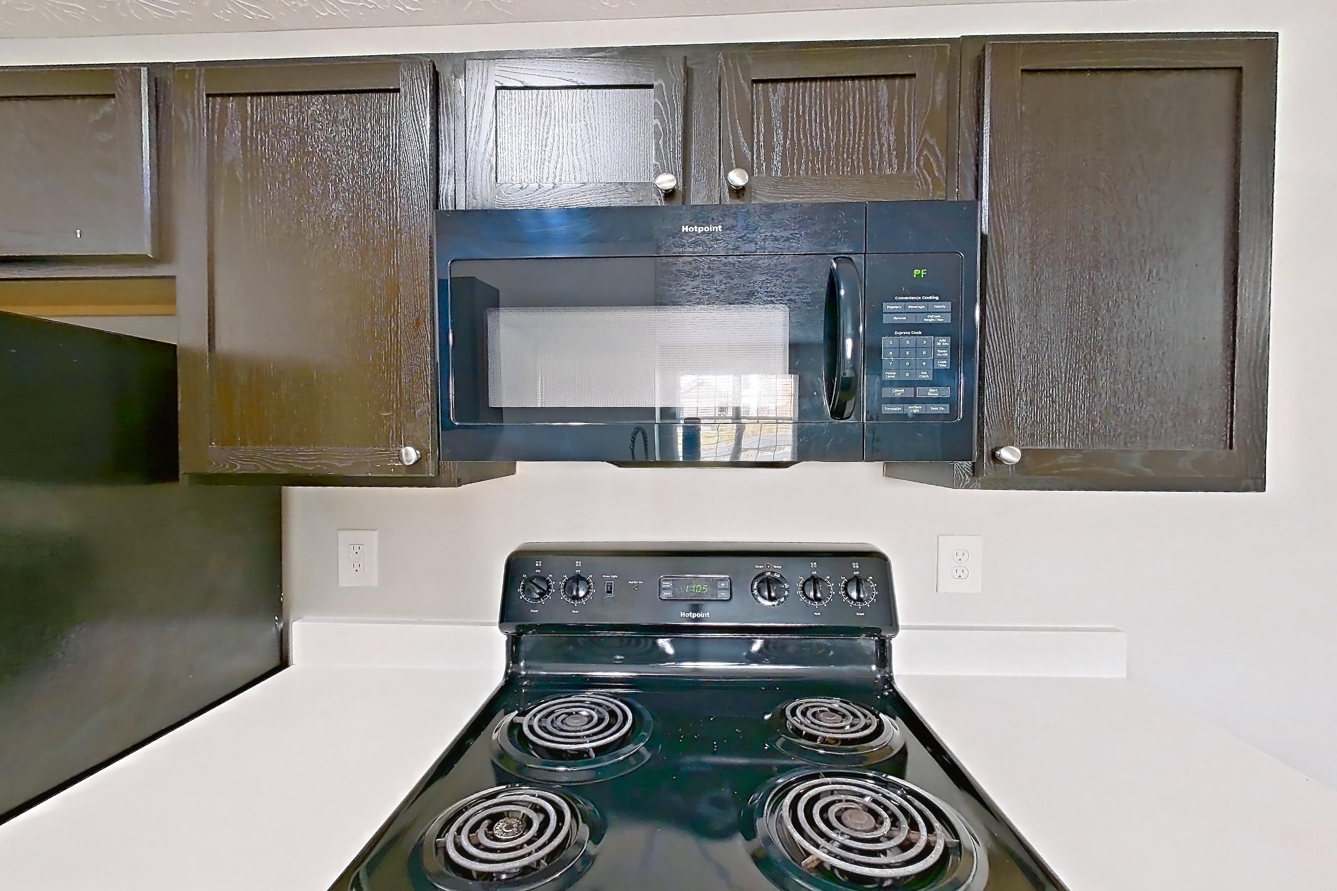 Kitchen with black appliances, dishwasher, electric range, light countertops, light wood-finish flooring, microwave, oven/range, refrigerator, and stainless steel appliances, Apartment 3642CCW at The Gardens Columbus