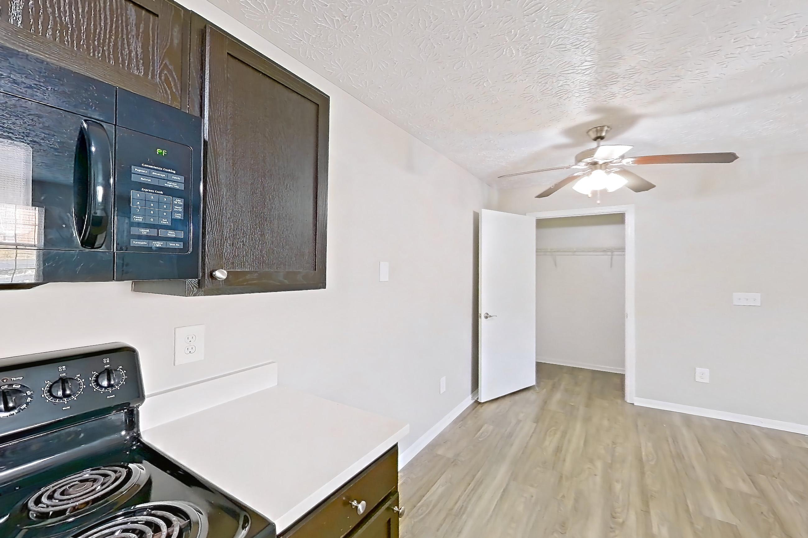 Kitchen with black appliances, dishwasher, electric range, light countertops, light wood-finish flooring, microwave, oven/range, refrigerator, and stainless steel appliances, Apartment 3642CCW at The Gardens Columbus