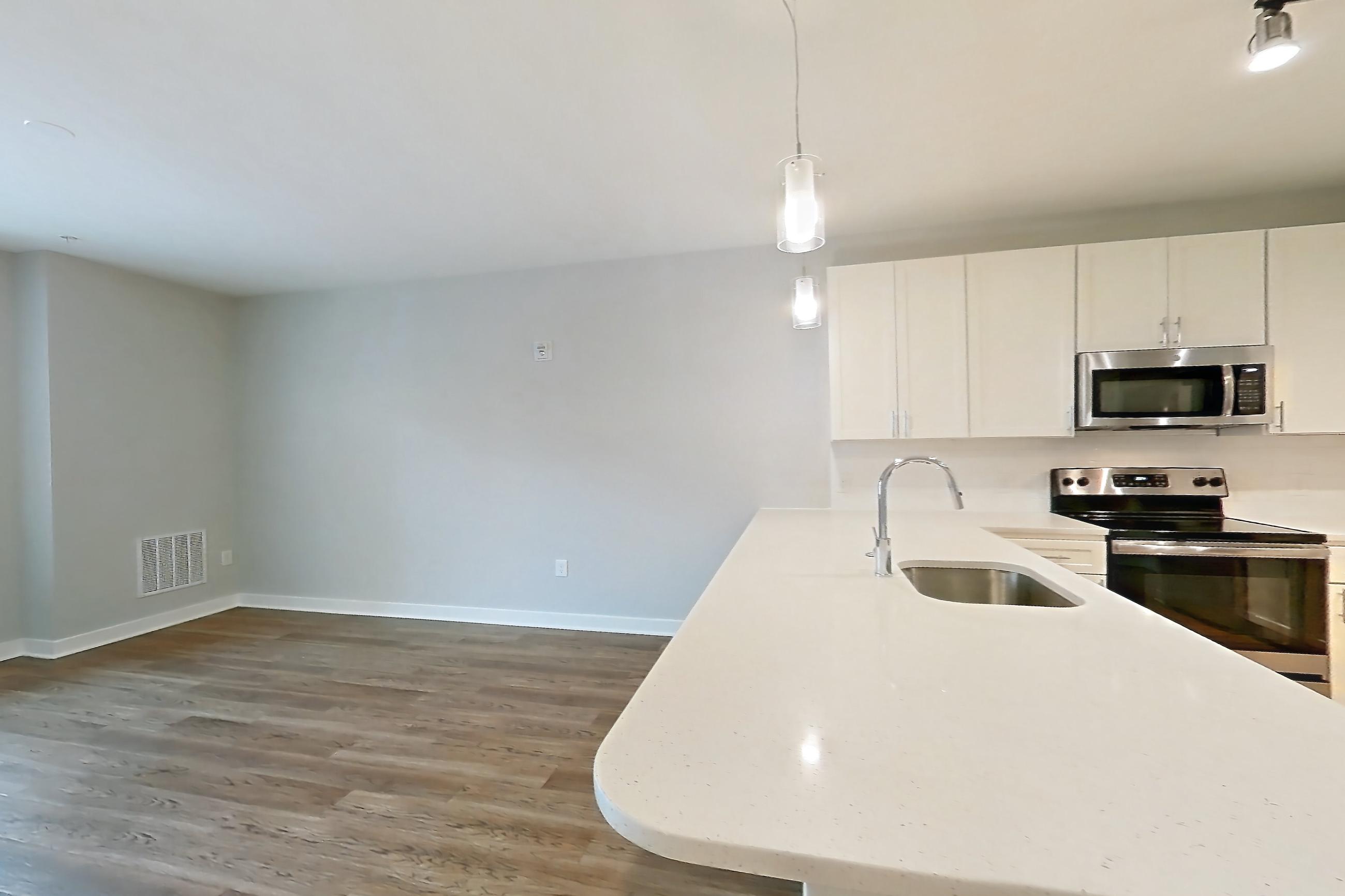 Living space with dark wood-finish flooring, electric range, light countertops, light stone countertops, light wood-finish flooring, microwave, oven/range, refrigerator, and stainless steel appliances, Apartment 18103 at Briggs & Union