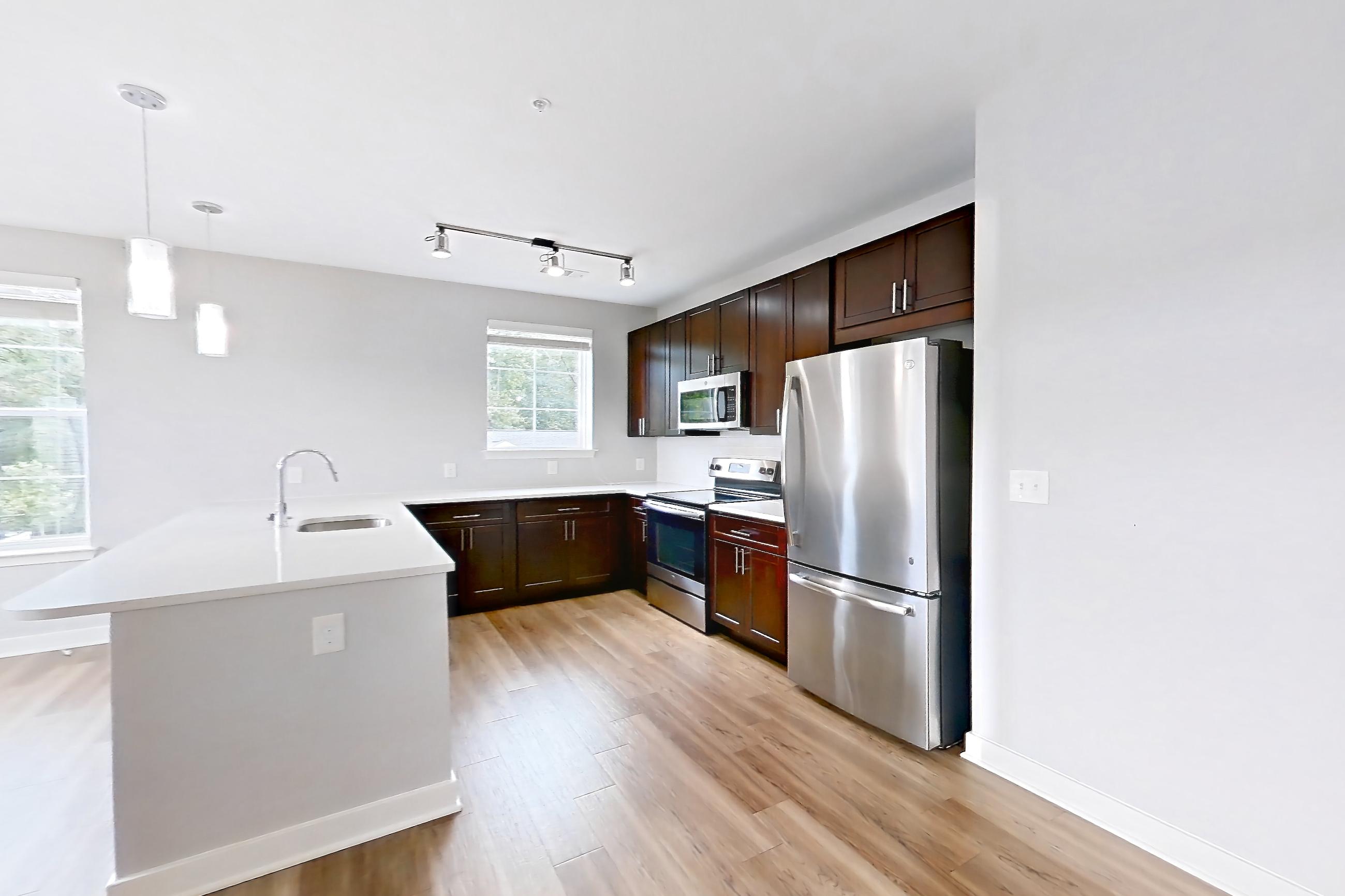 Living room with electric range, light countertops, light wood-finish flooring, microwave, oven/range, refrigerator, and stainless steel appliances, Apartment 13201 at Briggs & Union
