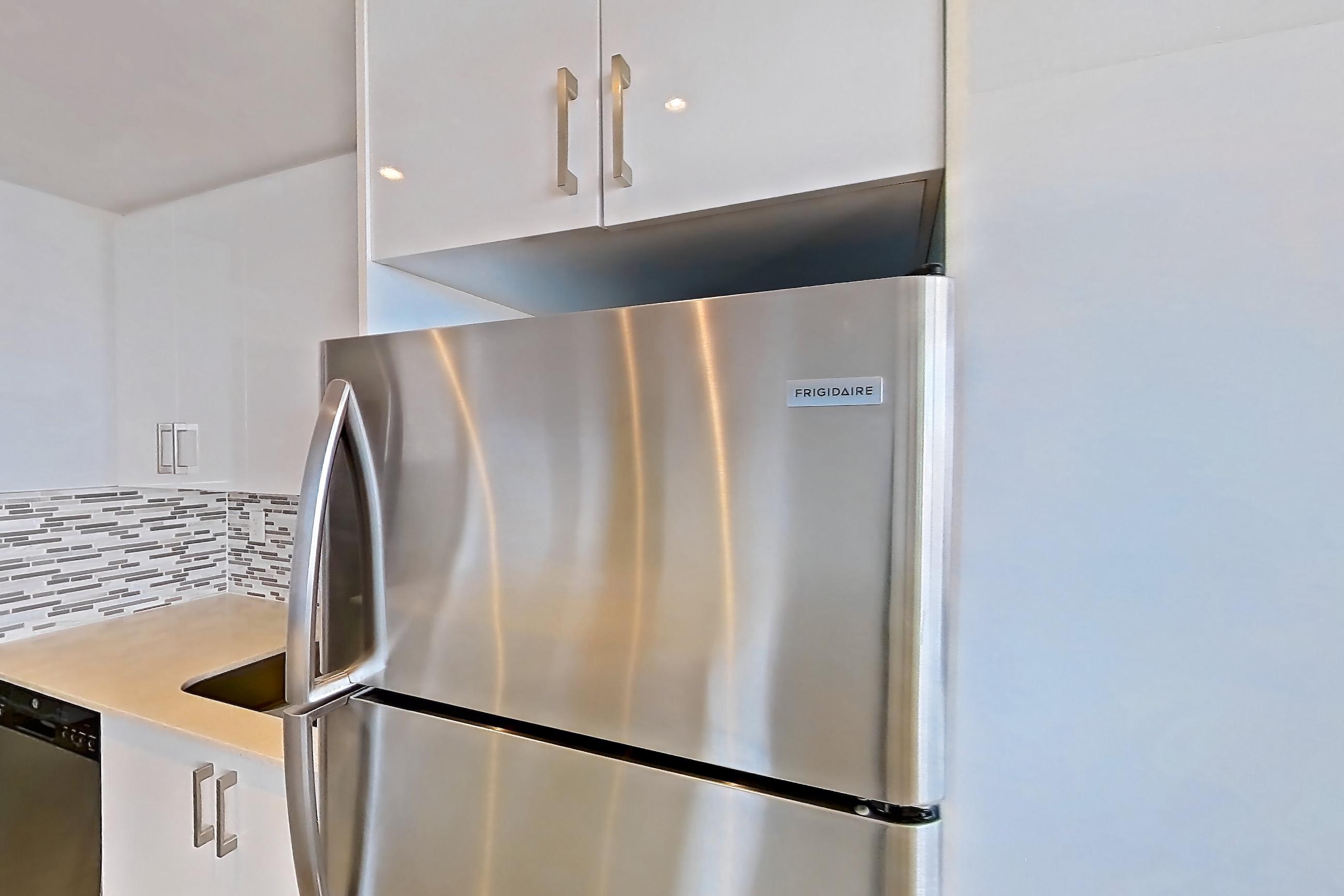 Kitchen with baseboard heating, dishwasher, electric range, light countertops, light tile flooring, light wood-finish flooring, oven/range, refrigerator, and stainless steel appliances, Apartment 0918 at 77 Davisville