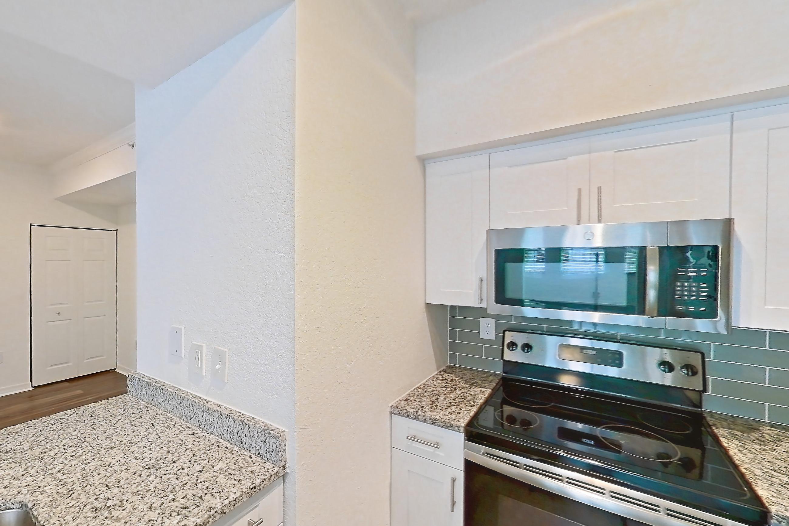 Kitchen with dark wood-finish flooring, dishwasher, electric range, light countertops, light stone countertops, light wood-finish flooring, microwave, oven/range, and stainless steel appliances, Apartment 12-204 at Solano at Miramar
