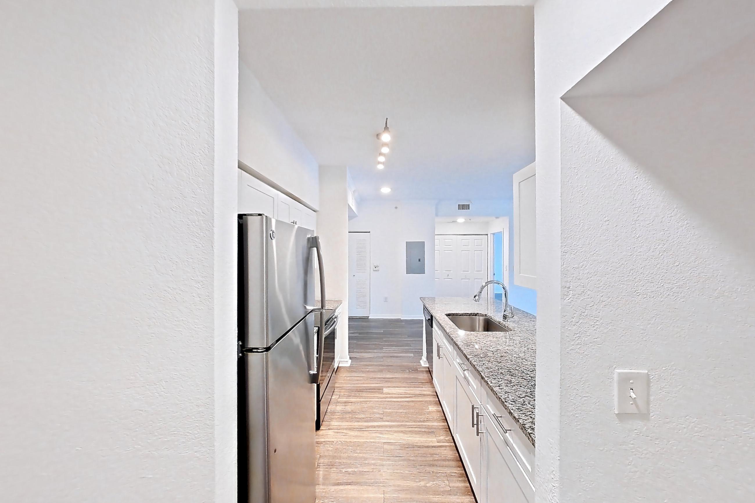 Entryway living space with dark wood-finish flooring, electric range, light stone countertops, oven/range, refrigerator, and stainless steel appliances, Apartment 01-208 at Solano at Miramar