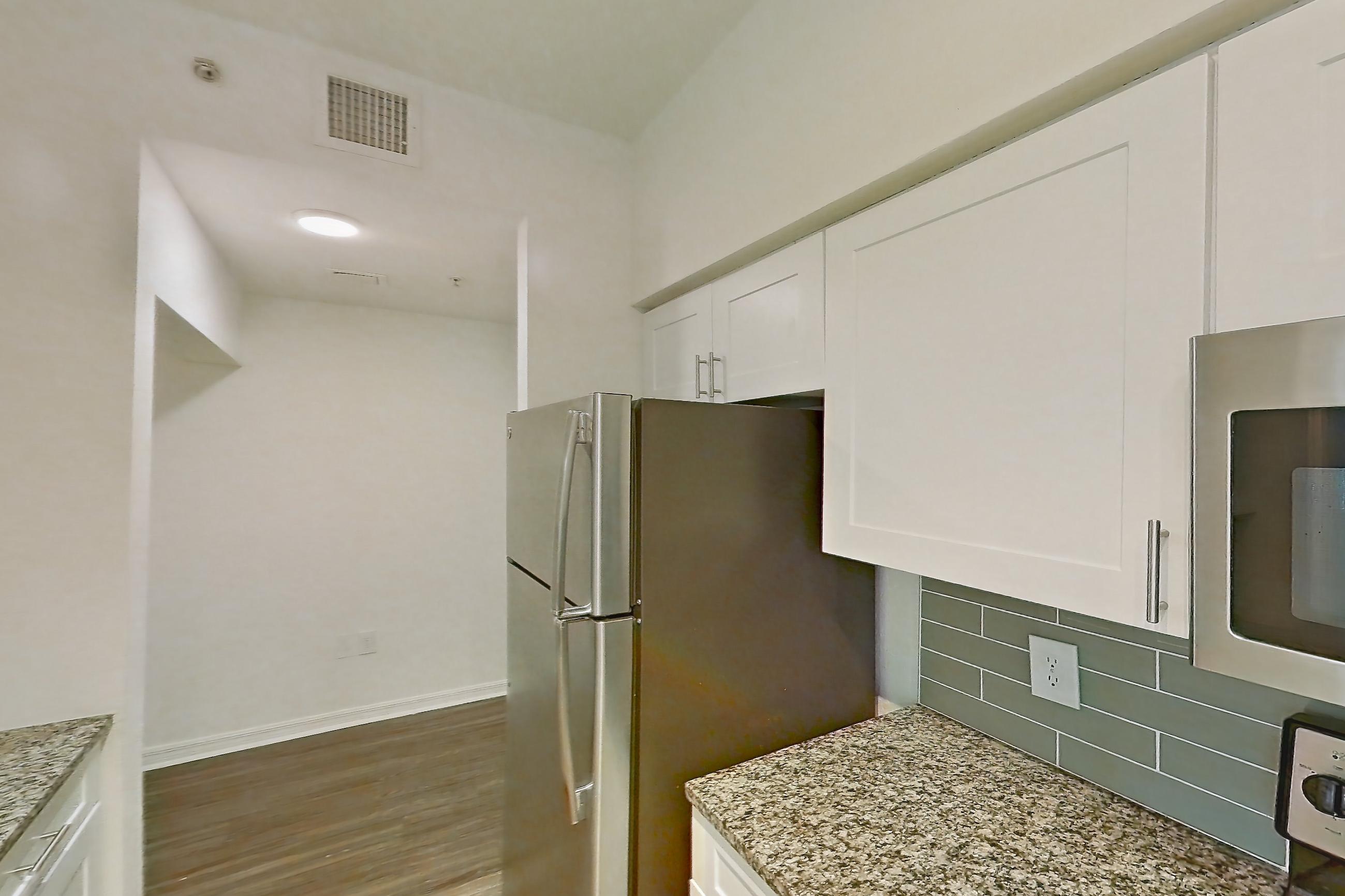 Kitchen with dishwasher, electric range, light countertops, light stone countertops, light wood-finish flooring, oven/range, refrigerator, and stainless steel appliances, Apartment 01-208 at Solano at Miramar