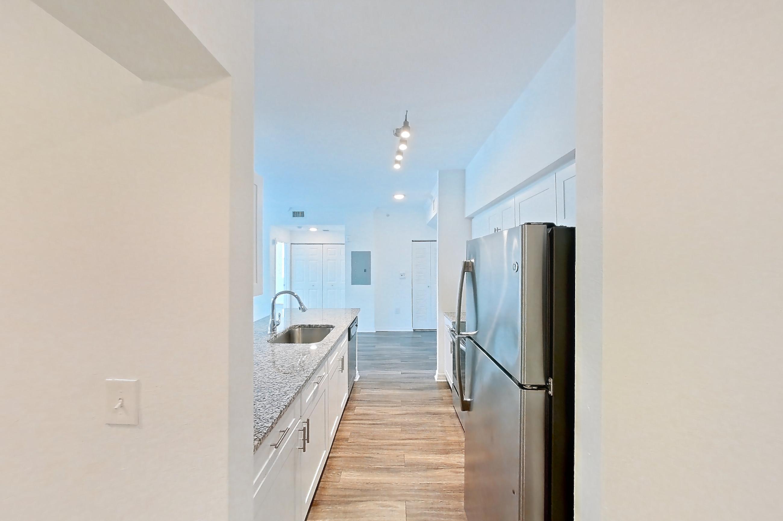 Entryway living space with dark wood-finish flooring, dishwasher, light countertops, light stone countertops, oven/range, refrigerator, and stainless steel appliances, Apartment 04-301 at Solano at Miramar