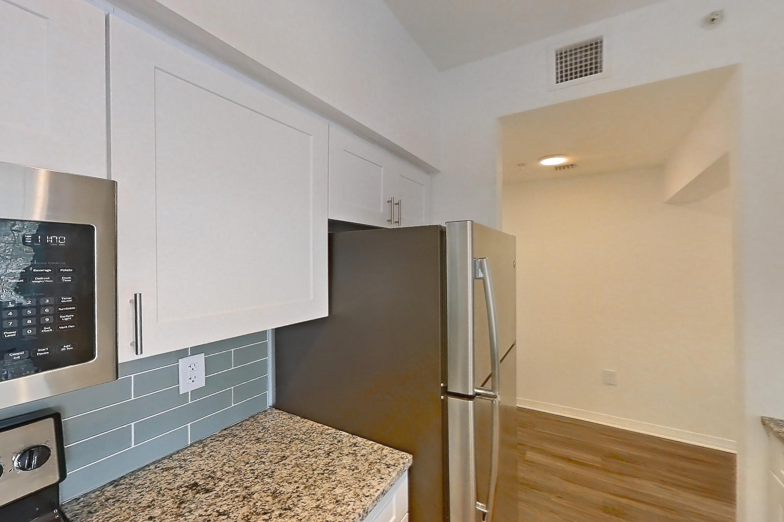 Kitchen with dishwasher, electric range, light countertops, light stone countertops, light wood-finish flooring, oven/range, refrigerator, and stainless steel appliances, Apartment 04-301 at Solano at Miramar