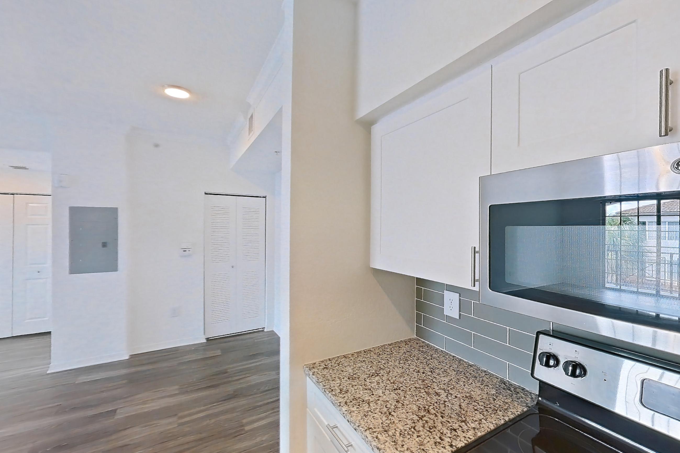 Kitchen with dishwasher, electric range, light countertops, light stone countertops, light wood-finish flooring, oven/range, refrigerator, and stainless steel appliances, Apartment 04-301 at Solano at Miramar