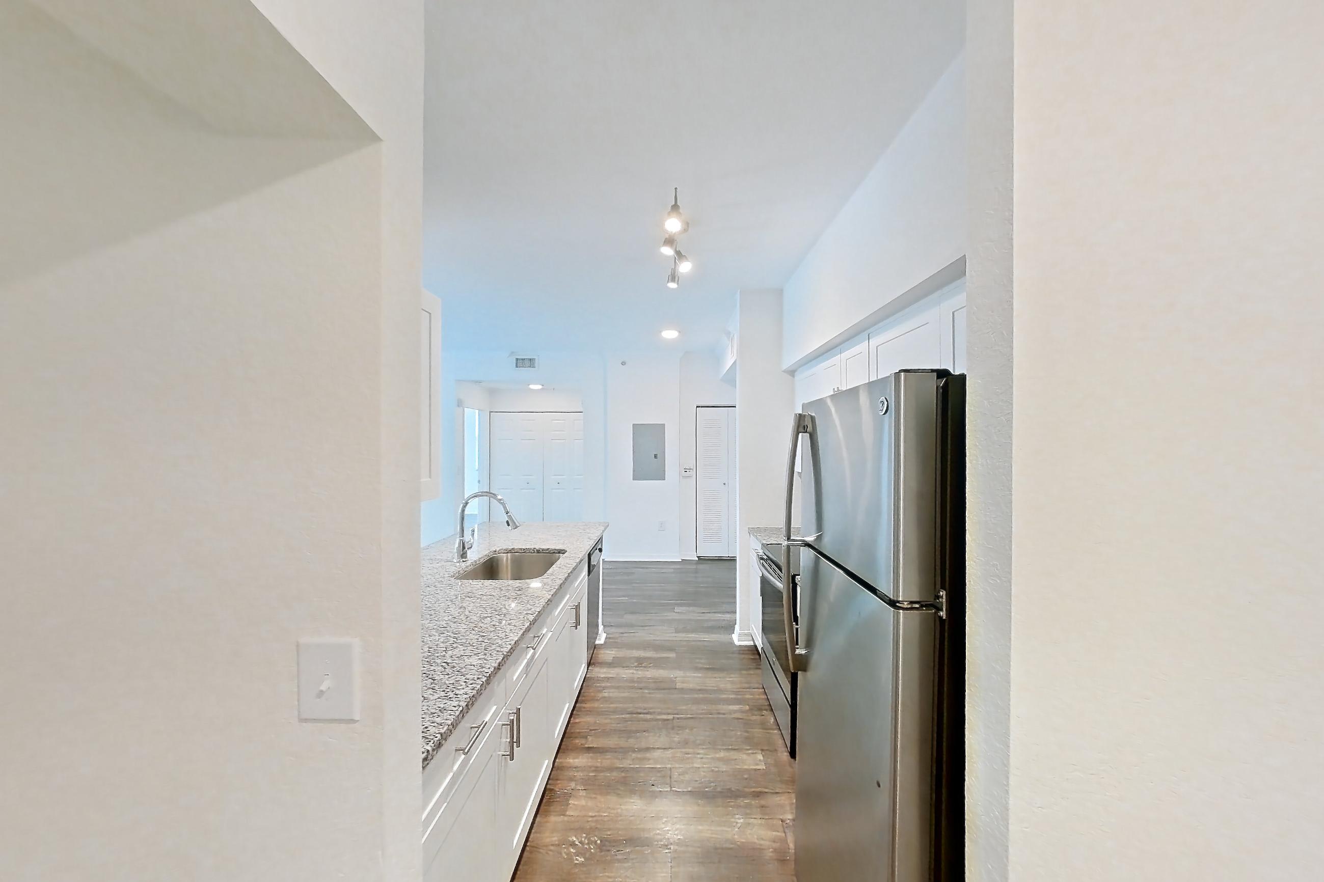 Entryway living space with dark wood-finish flooring, electric range, light countertops, light stone countertops, oven/range, refrigerator, and stainless steel appliances, Apartment 05-201 at Solano at Miramar