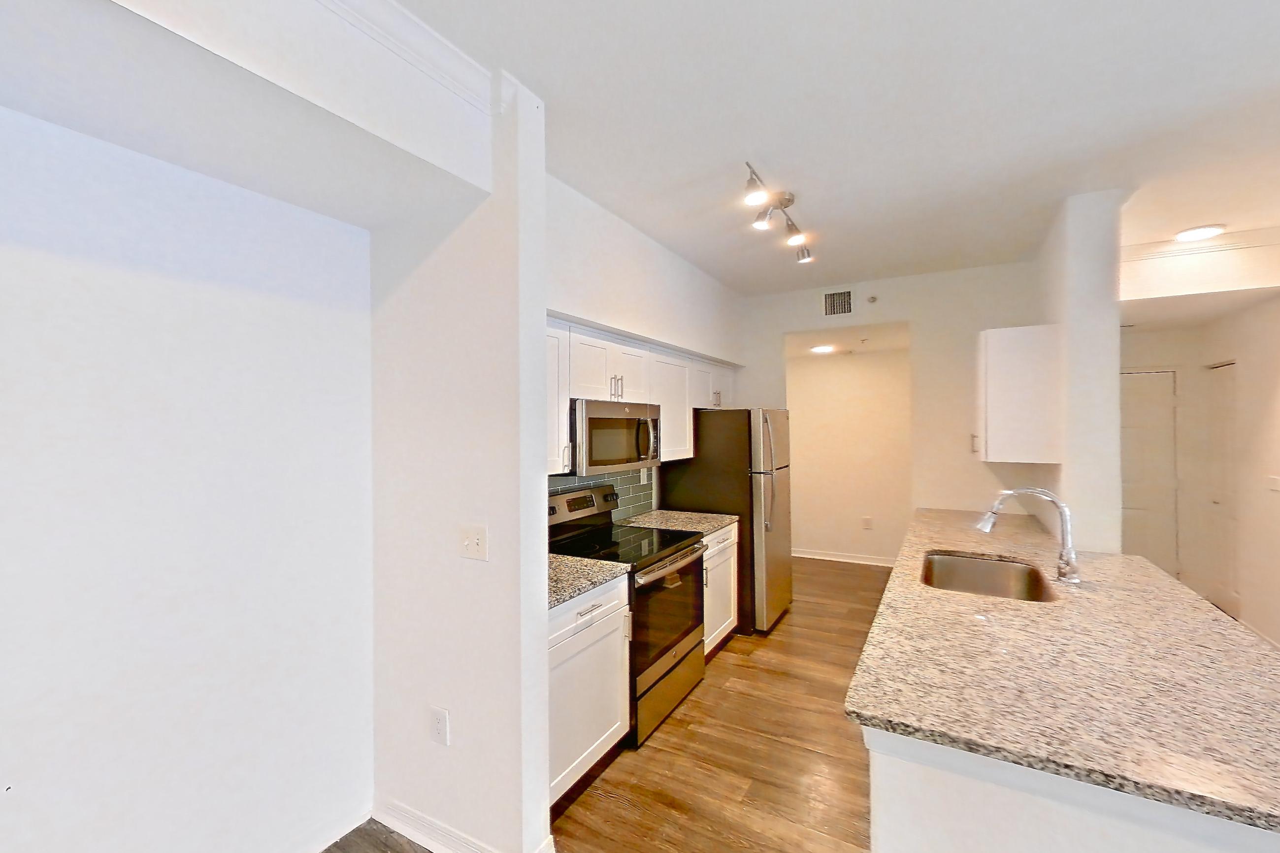 Living space with dark wood-finish flooring, electric range, kitchen island, light stone countertops, oven/range, refrigerator, and stainless steel appliances, Apartment 05-201 at Solano at Miramar