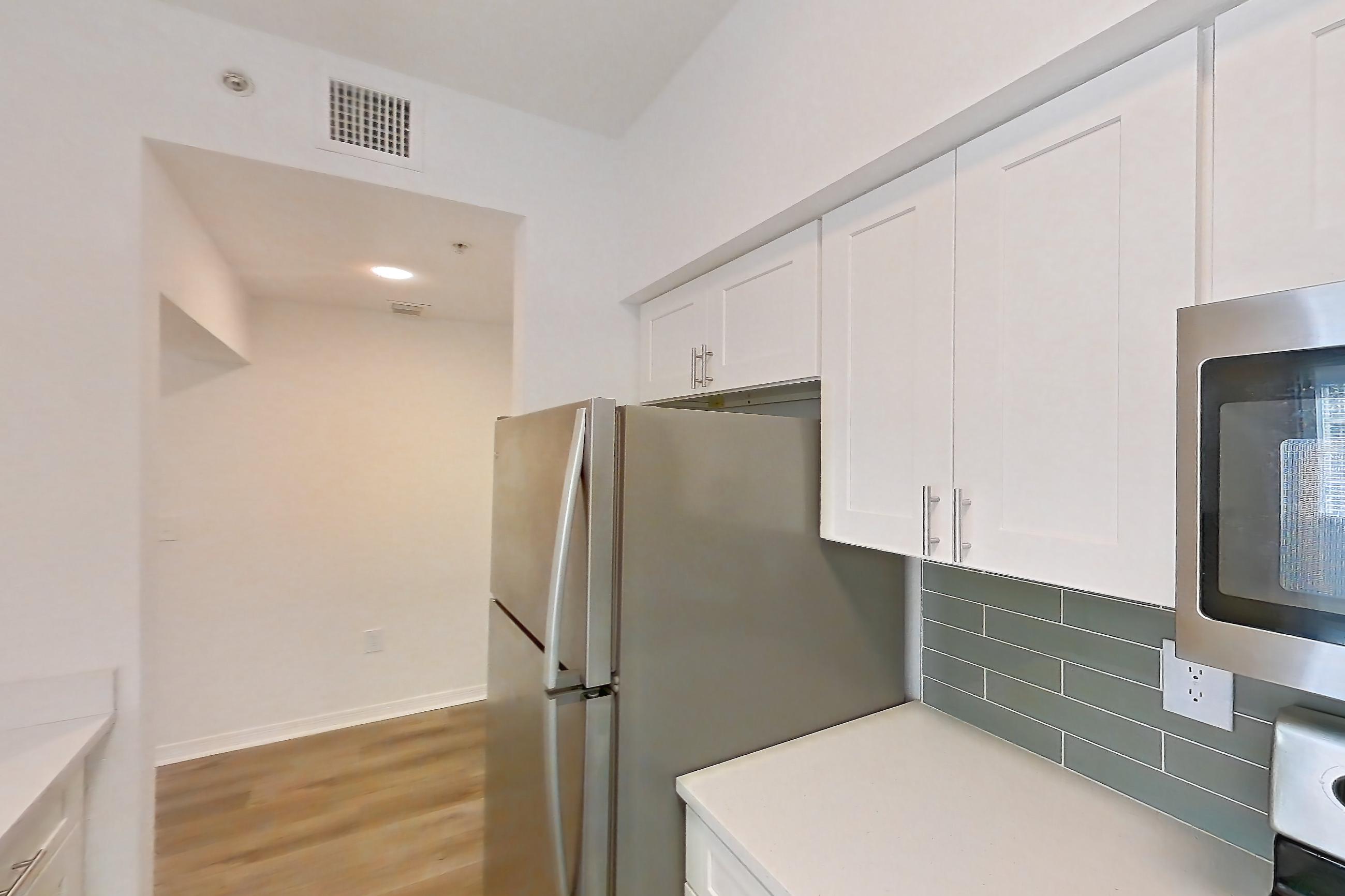 Kitchen with dishwasher, electric range, light countertops, light stone countertops, light wood-finish flooring, oven/range, refrigerator, and stainless steel appliances, Apartment 11-208 at Solano at Miramar