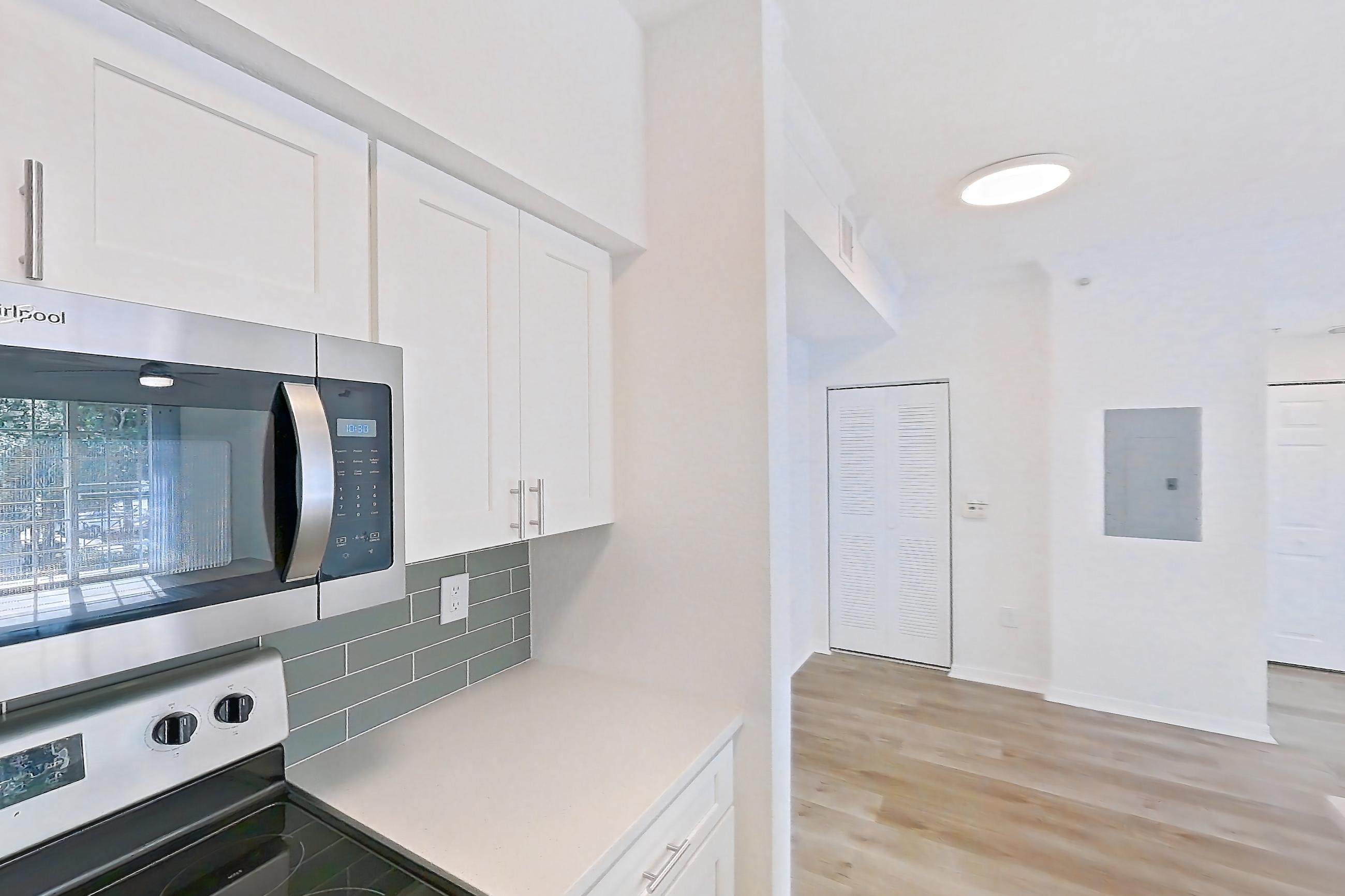 Kitchen with dishwasher, electric range, light countertops, light stone countertops, light wood-finish flooring, oven/range, refrigerator, and stainless steel appliances, Apartment 11-208 at Solano at Miramar