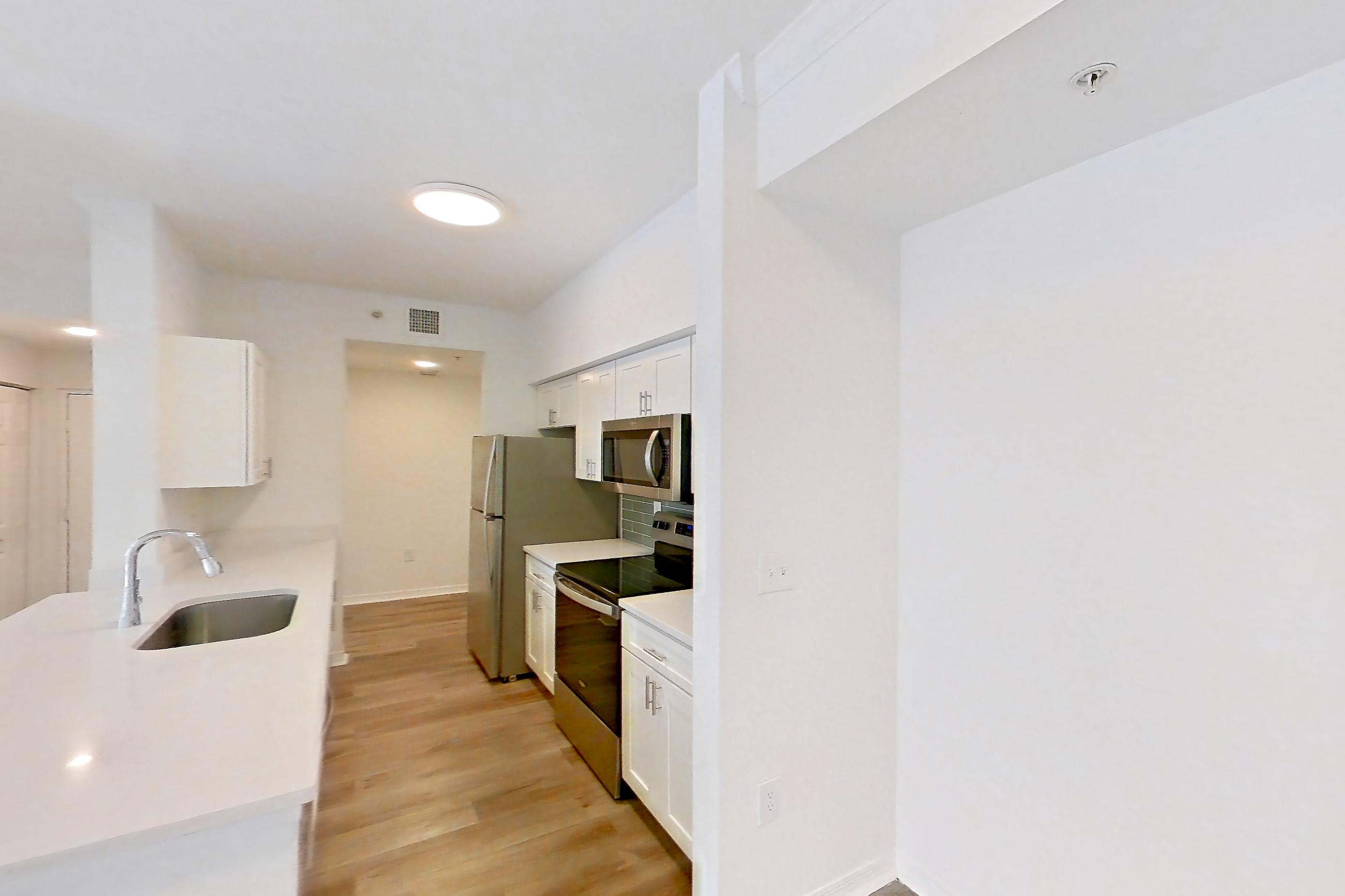 Main living space with electric range, light stone countertops, light wood-finish flooring, microwave, oven/range, refrigerator, and stainless steel appliances, Apartment 11-208 at Solano at Miramar