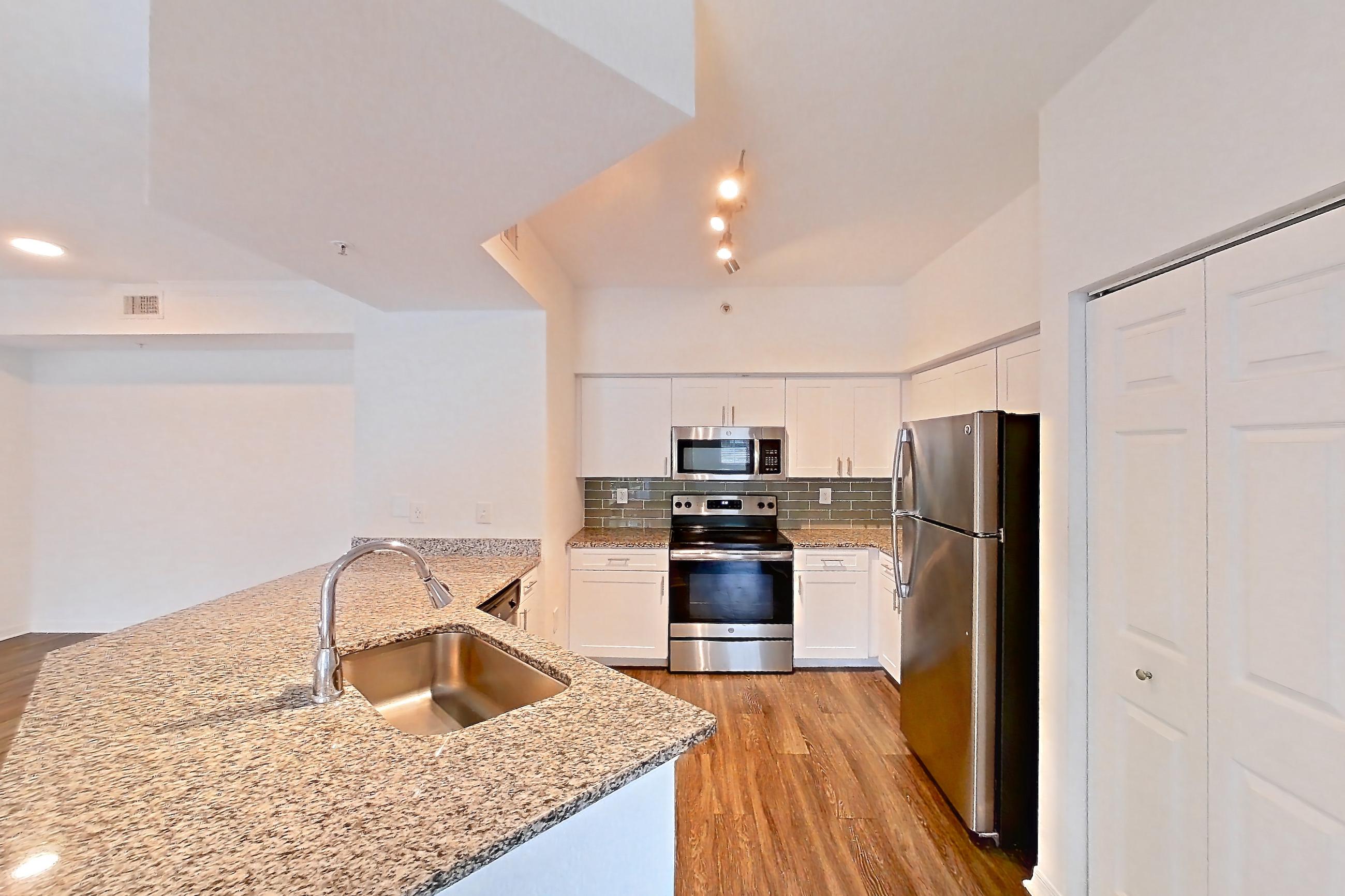 Kitchen entryway with dark wood-finish flooring, electric range, light stone countertops, oven/range, refrigerator, and stainless steel appliances, Apartment 06-107 at Solano at Miramar