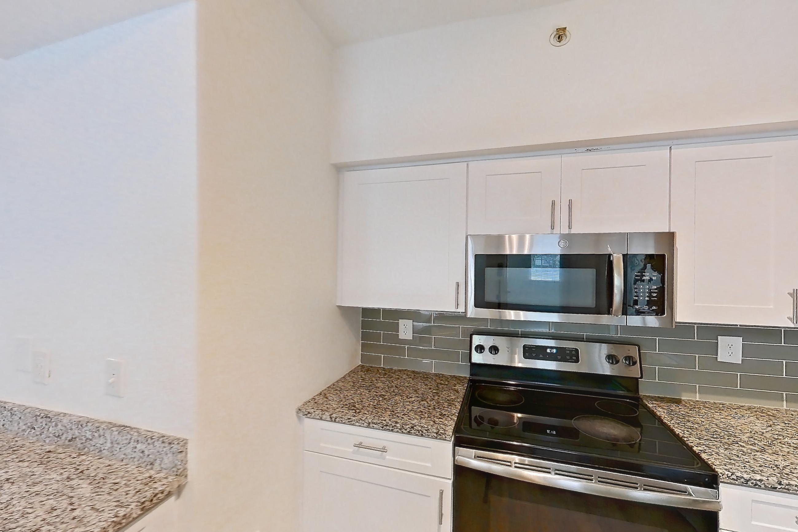 Kitchen with dark wood-finish flooring, dishwasher, electric range, light stone countertops, light wood-finish flooring, microwave, oven/range, refrigerator, and stainless steel appliances, Apartment 06-107 at Solano at Miramar