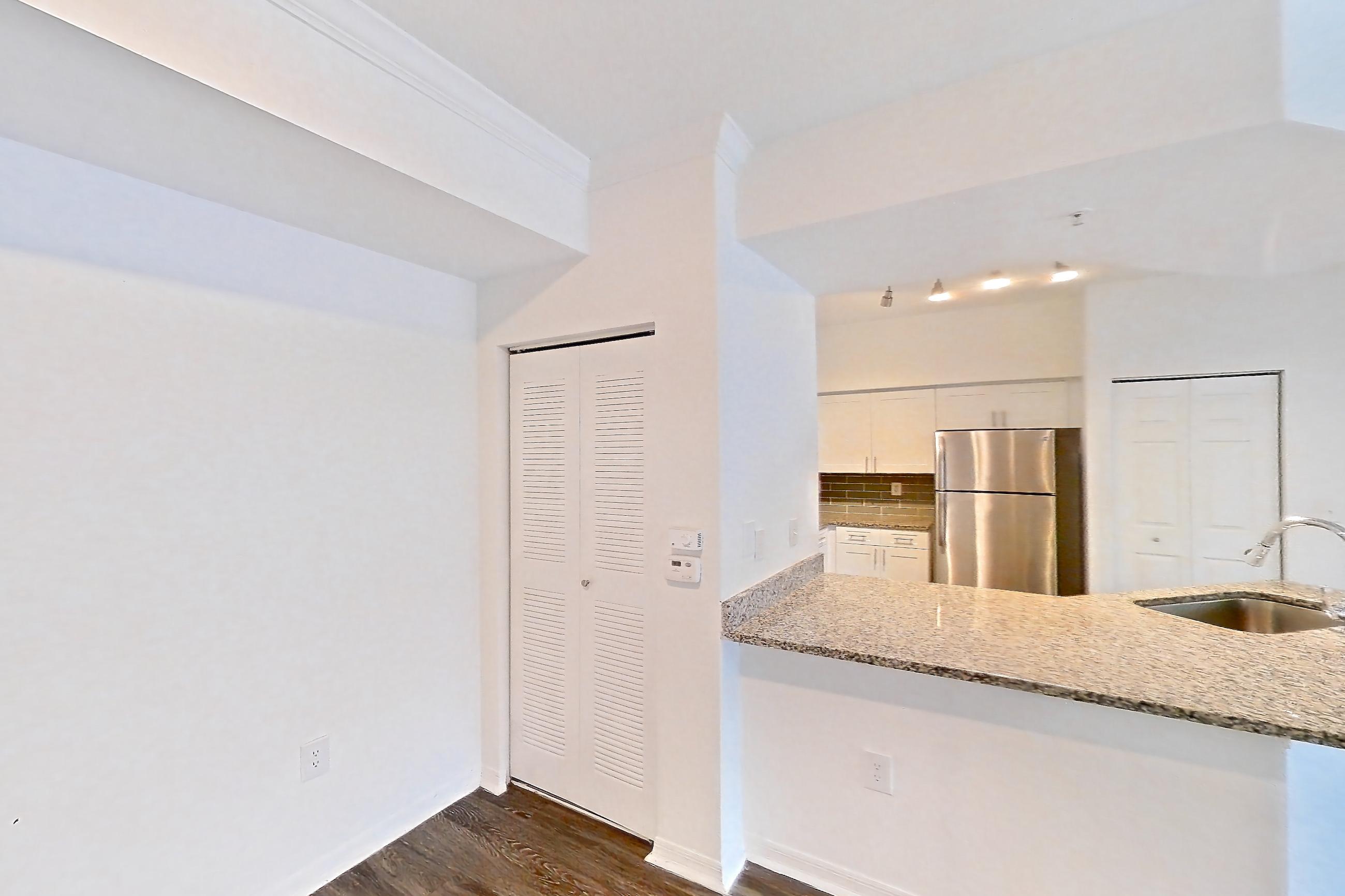 Living space with dark wood-finish flooring, light stone countertops, refrigerator, and stainless steel appliances, Apartment 06-107 at Solano at Miramar