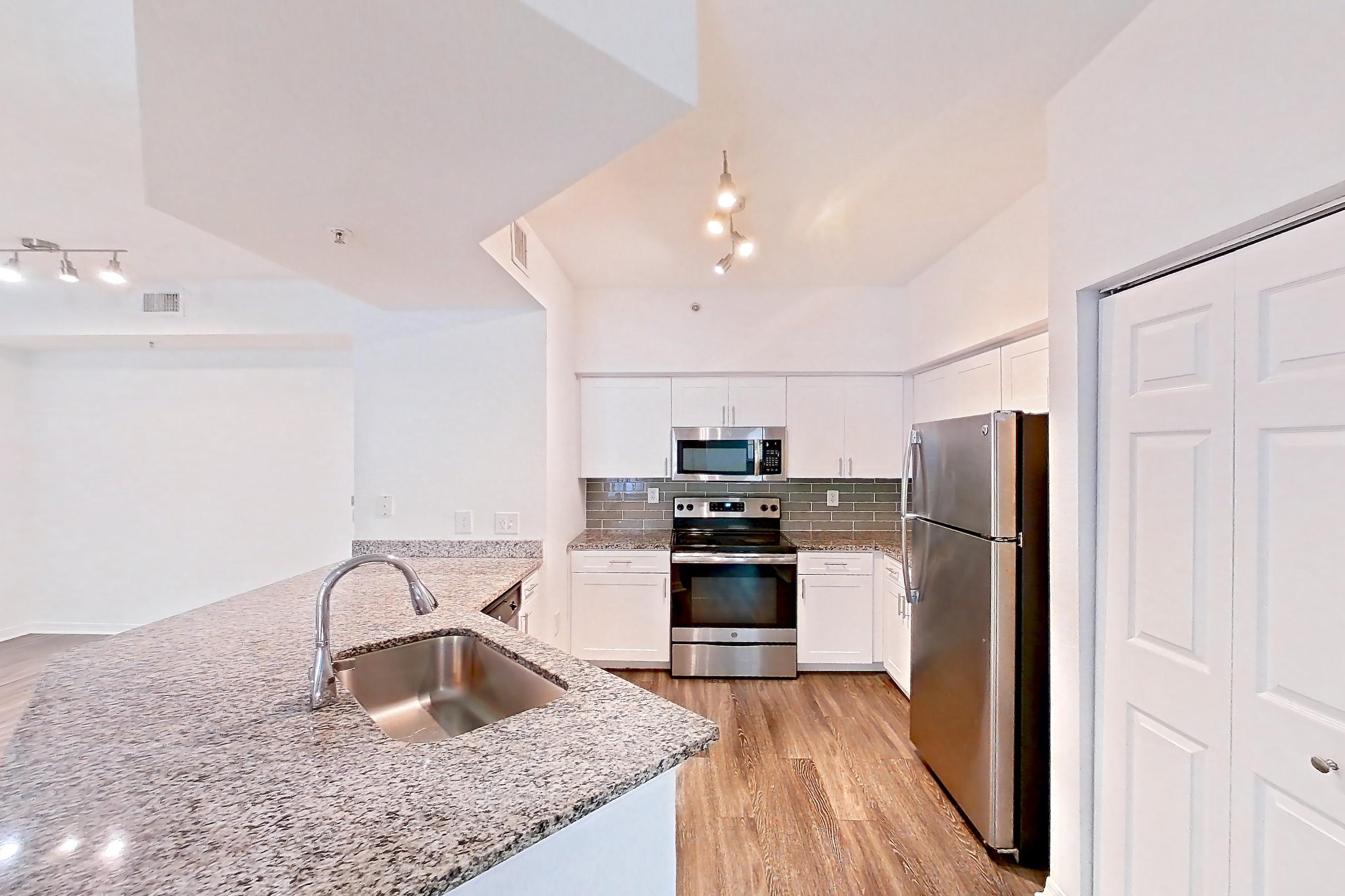 Kitchen entryway with dark wood-finish flooring, electric range, light stone countertops, oven/range, refrigerator, and stainless steel appliances, Apartment 05-103 at Solano at Miramar
