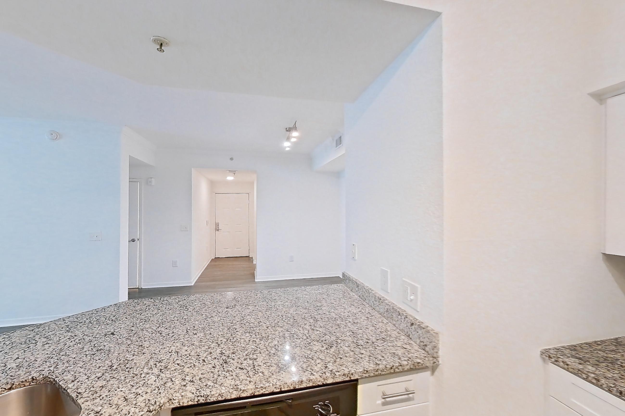 Kitchen with dark wood-finish flooring, dishwasher, electric range, light stone countertops, microwave, oven/range, refrigerator, and stainless steel appliances, Apartment 05-103 at Solano at Miramar