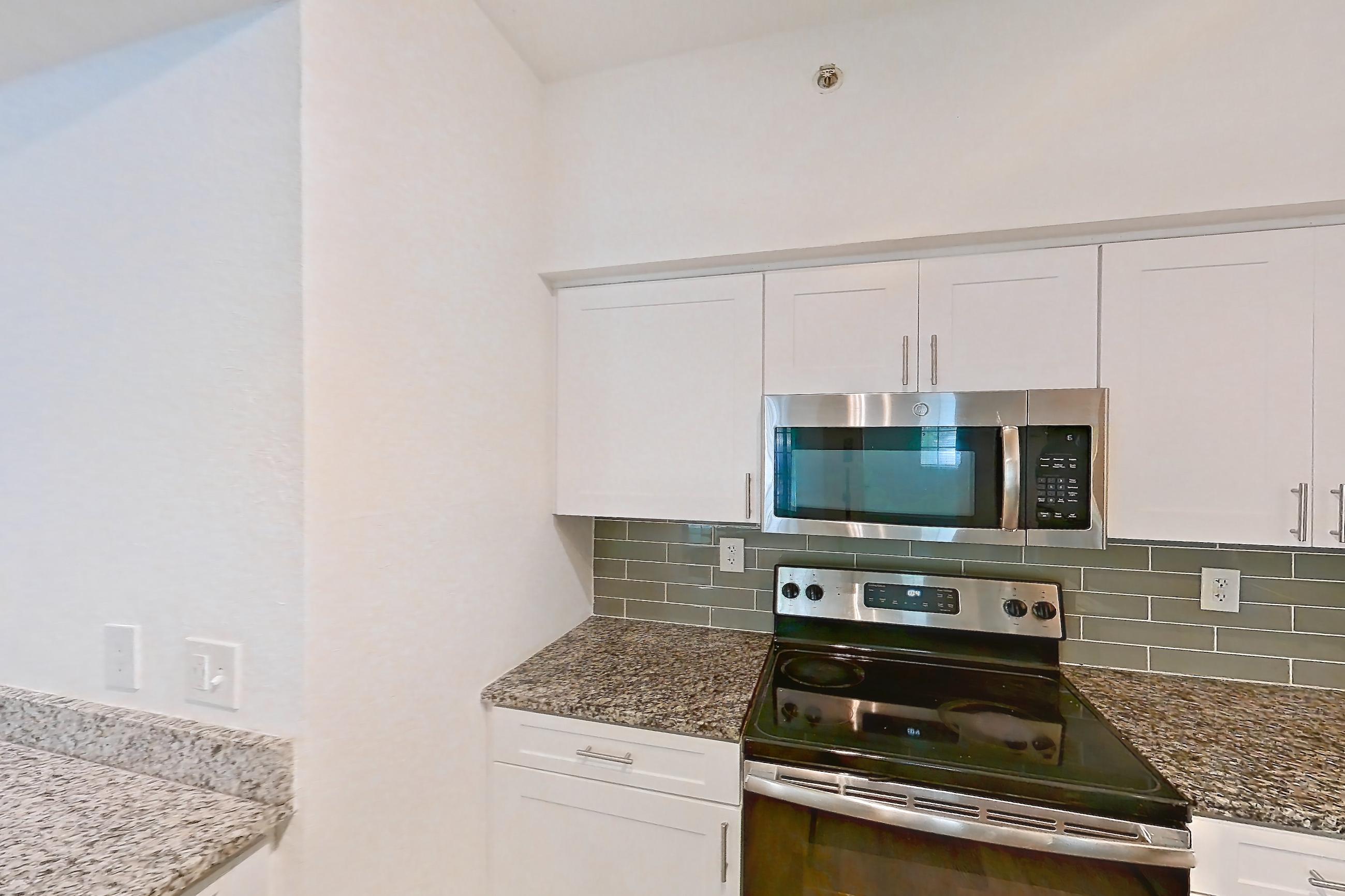 Kitchen with dark wood-finish flooring, dishwasher, electric range, light stone countertops, microwave, oven/range, refrigerator, and stainless steel appliances, Apartment 05-103 at Solano at Miramar