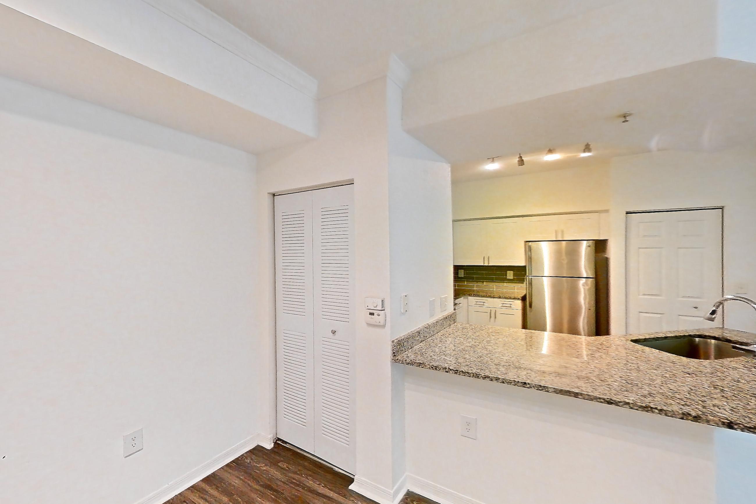 Living space with dark wood-finish flooring, light stone countertops, refrigerator, and stainless steel appliances, Apartment 05-103 at Solano at Miramar