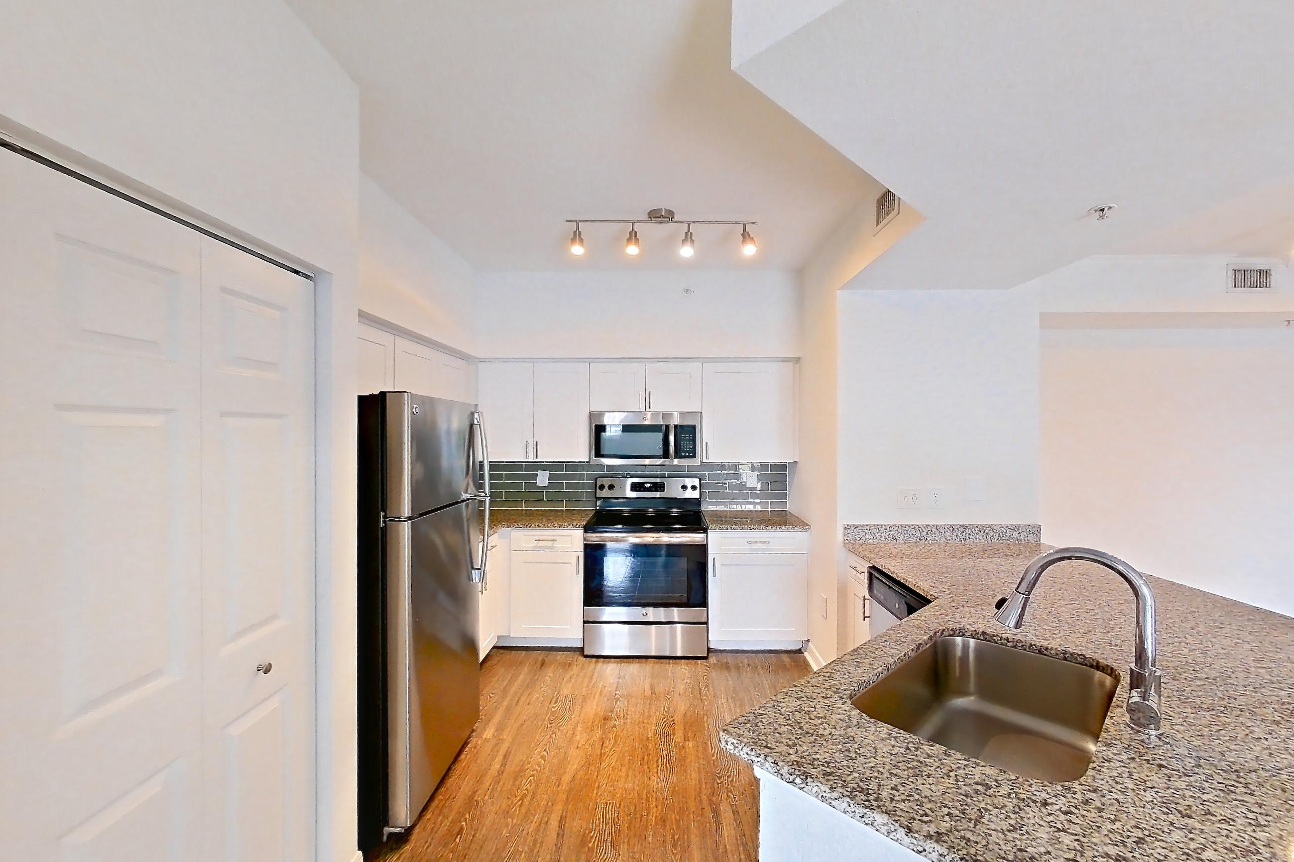 Kitchen entryway with dark wood-finish flooring, dishwasher, electric range, light stone countertops, oven/range, refrigerator, and stainless steel appliances, Apartment 08-110 at Solano at Miramar